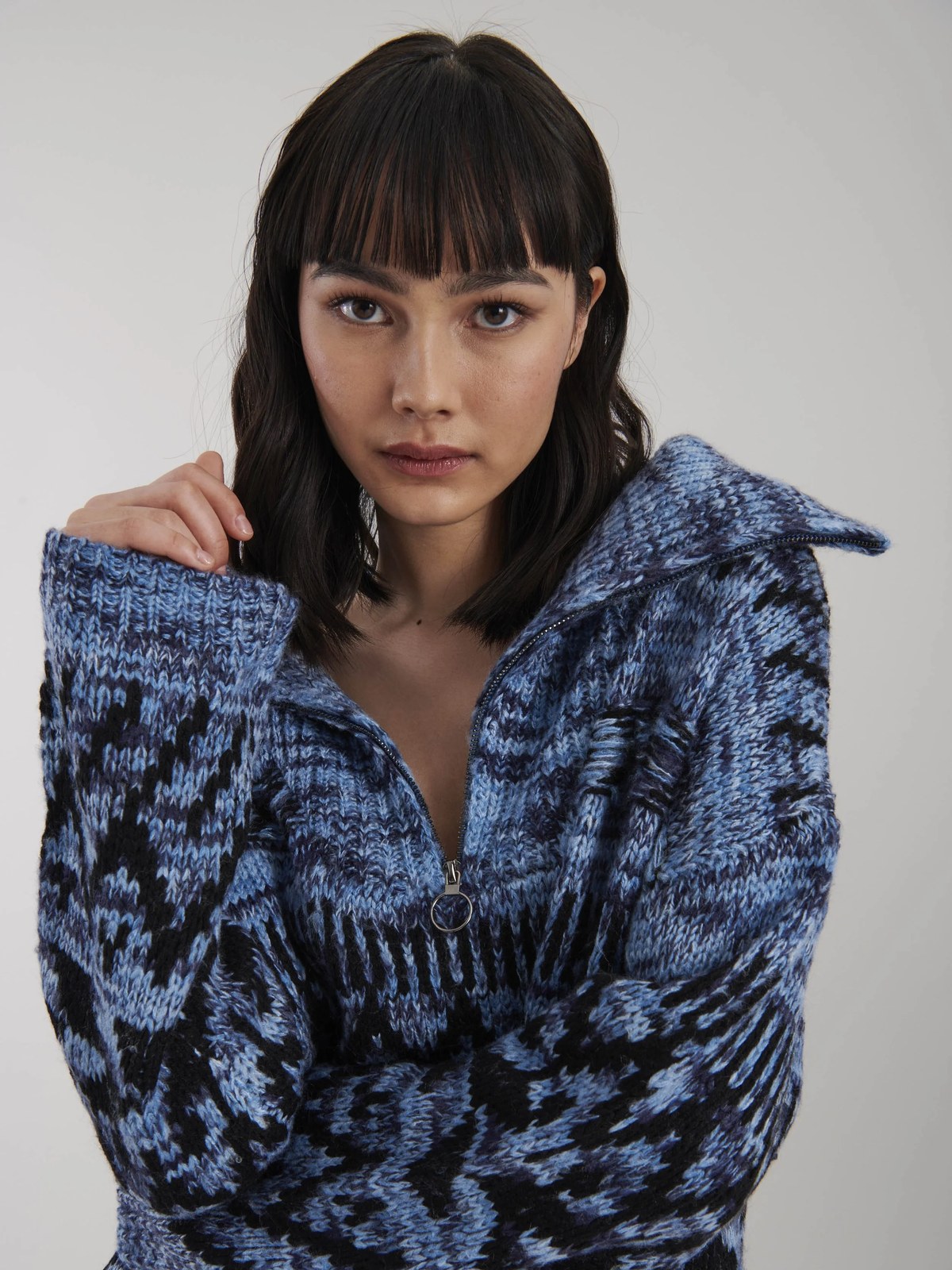Model in a blue patterned knit holding its collar near her face