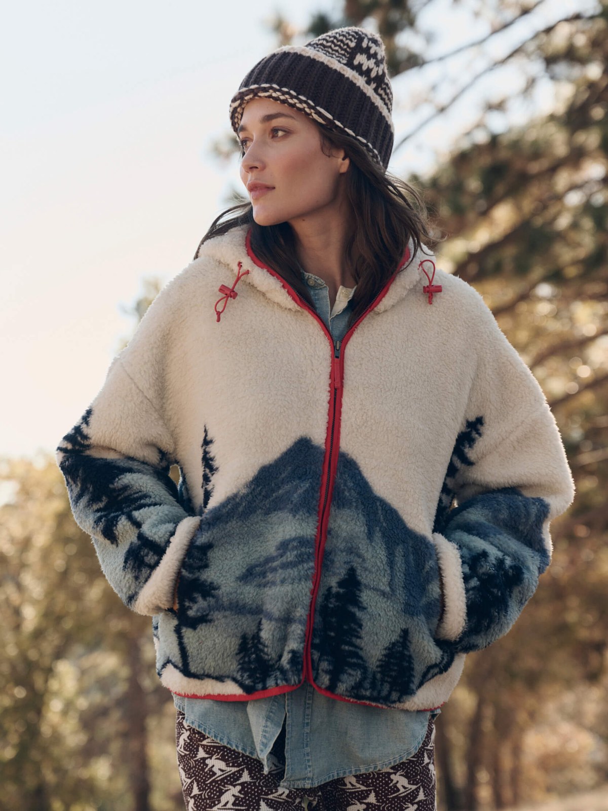 Model in a fleece jacket and knit hat against a forest background