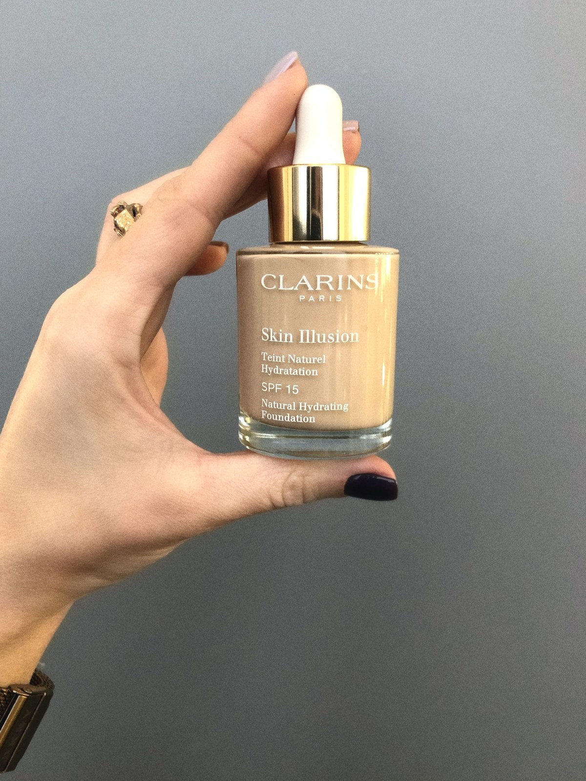 Hand holding a bottle of Clarins Skin Illusion Foundation against a grey background