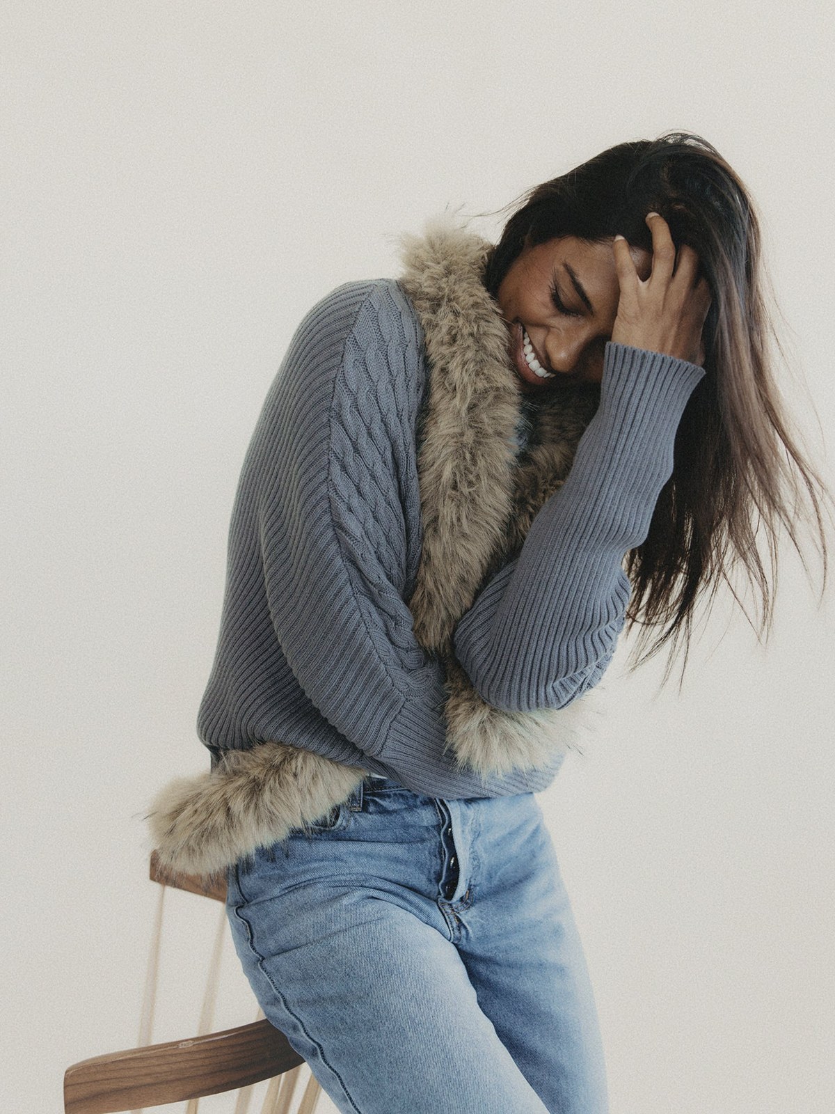 Model in a gray cable knit and light jeans with fur-trimmed sleeves