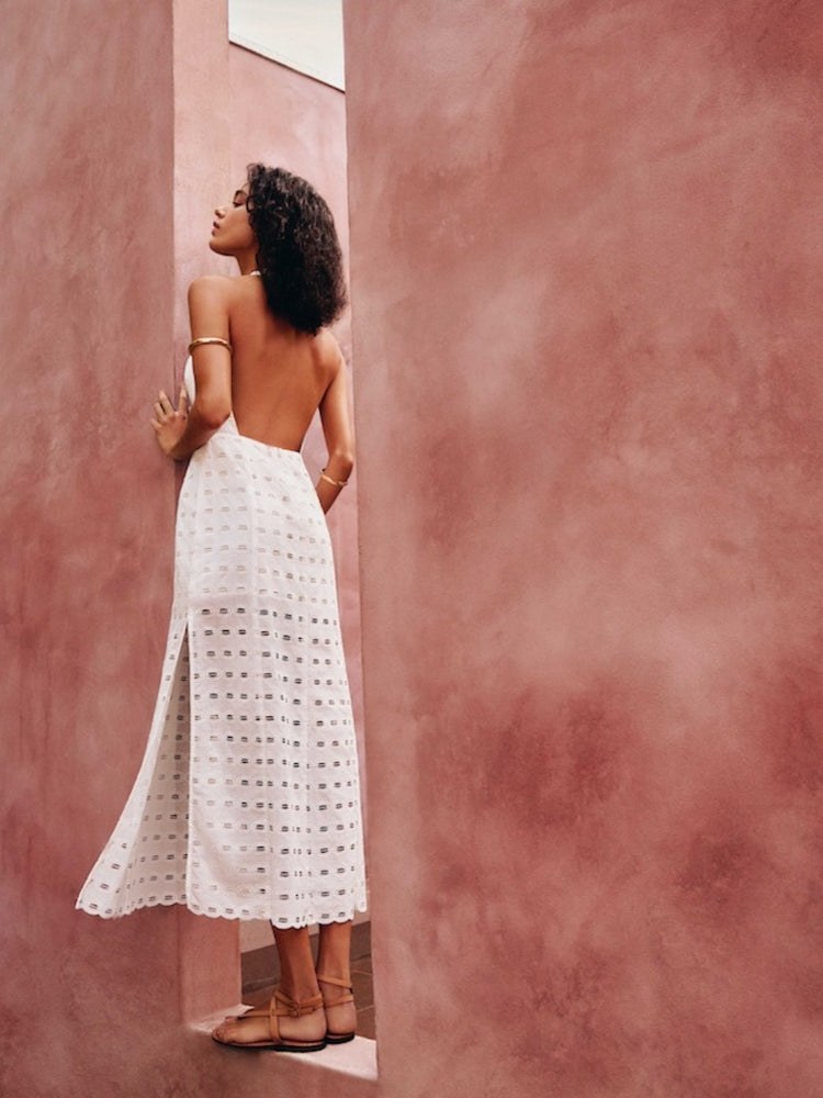 Woman in a white eyelet resort dress against a rose-colored wall