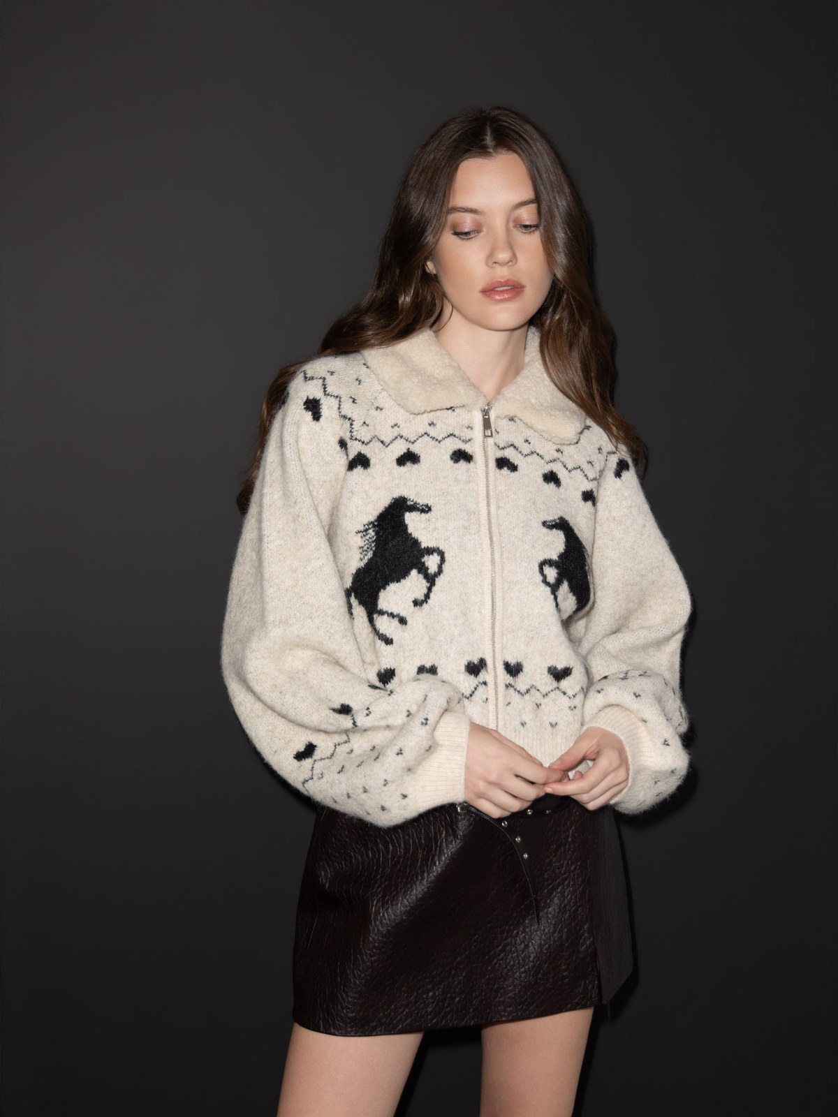 Model in a patterned knit and black skirt against a dark studio backdrop