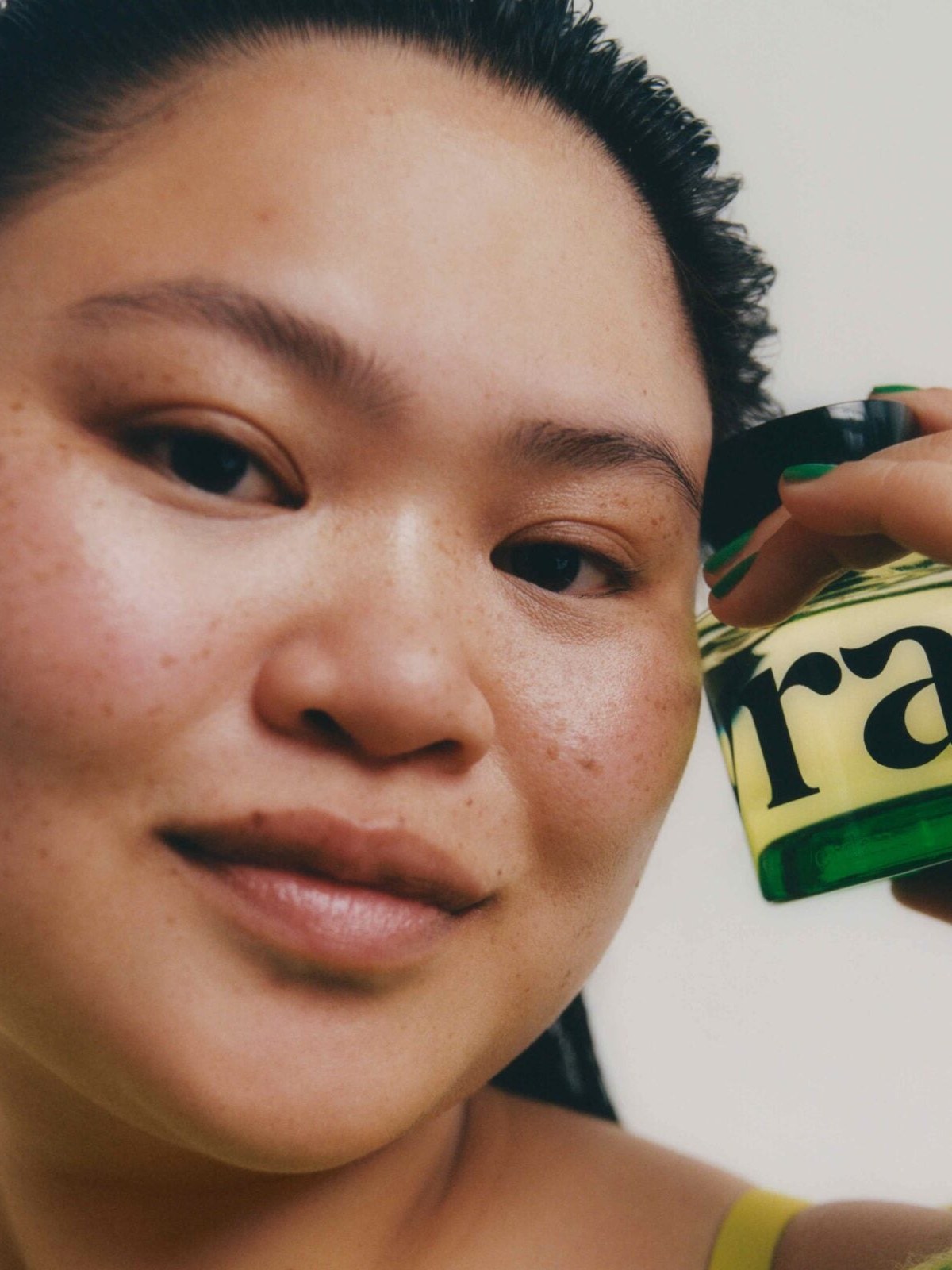 Model in a green top holding a perfume bottle