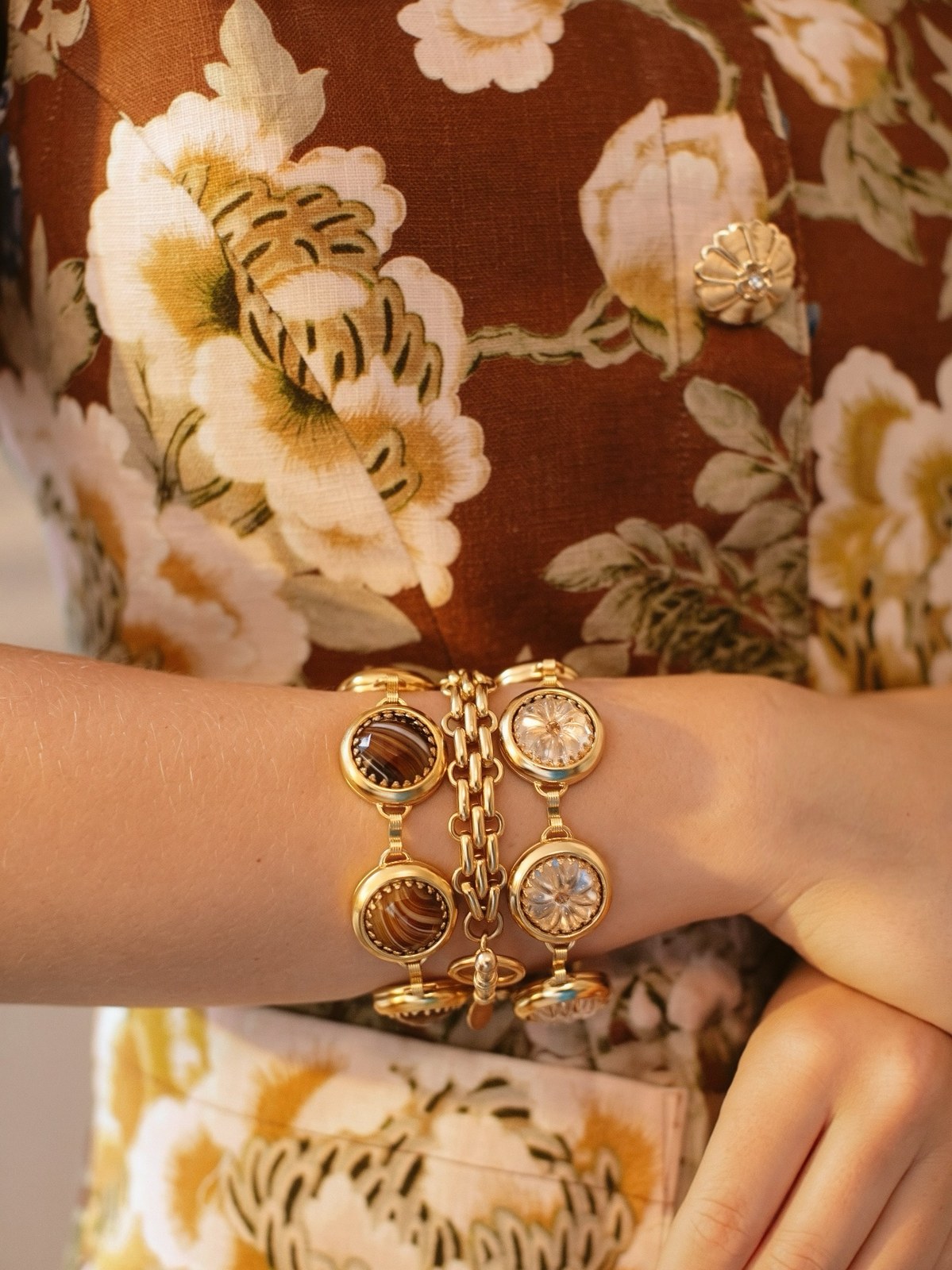Wrist in a floral sleeve stacked with gold-and-stone charm bracelets