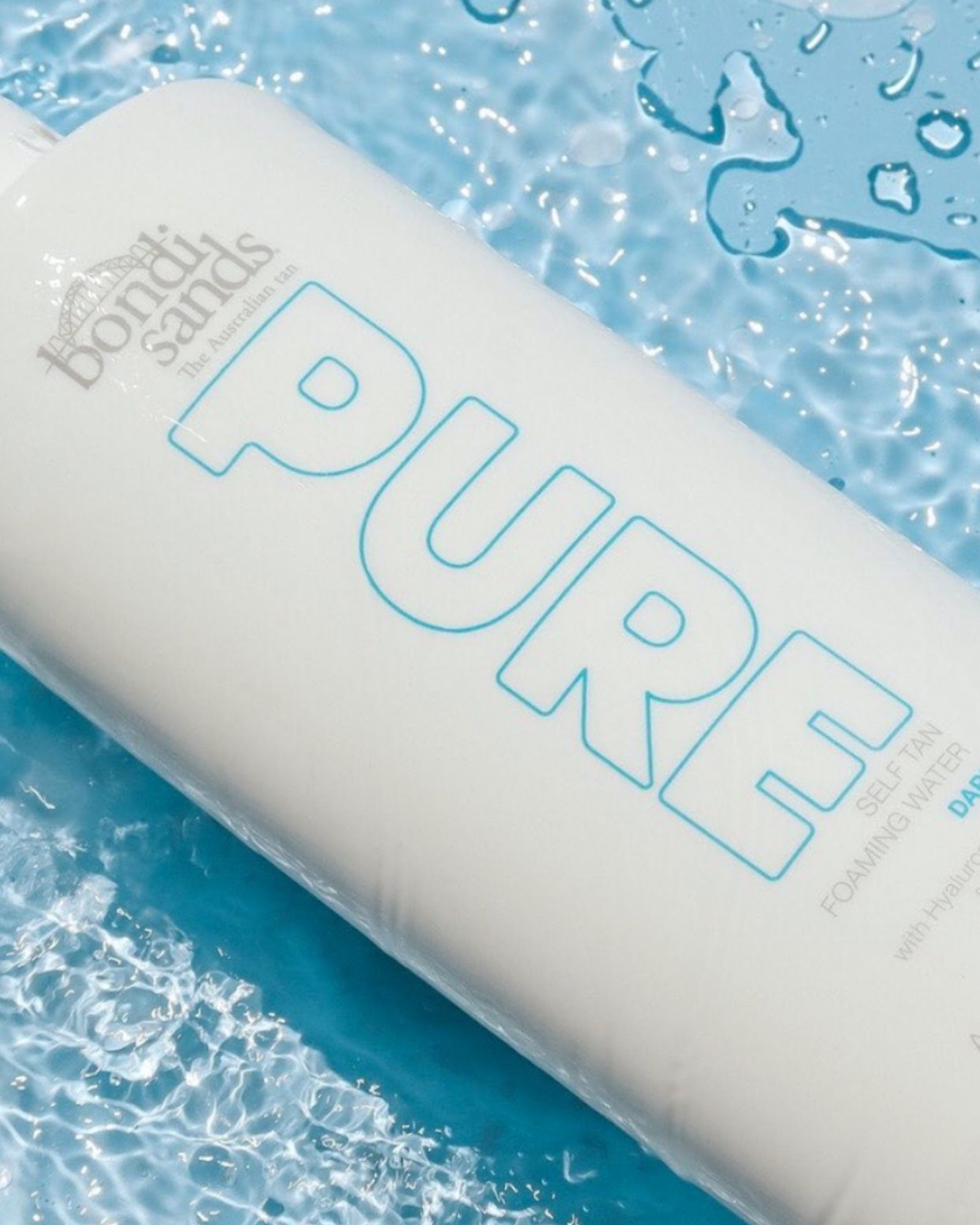 Bondi Sands Pure Self Tan Foaming Water bottle lying in clear blue water with splashes