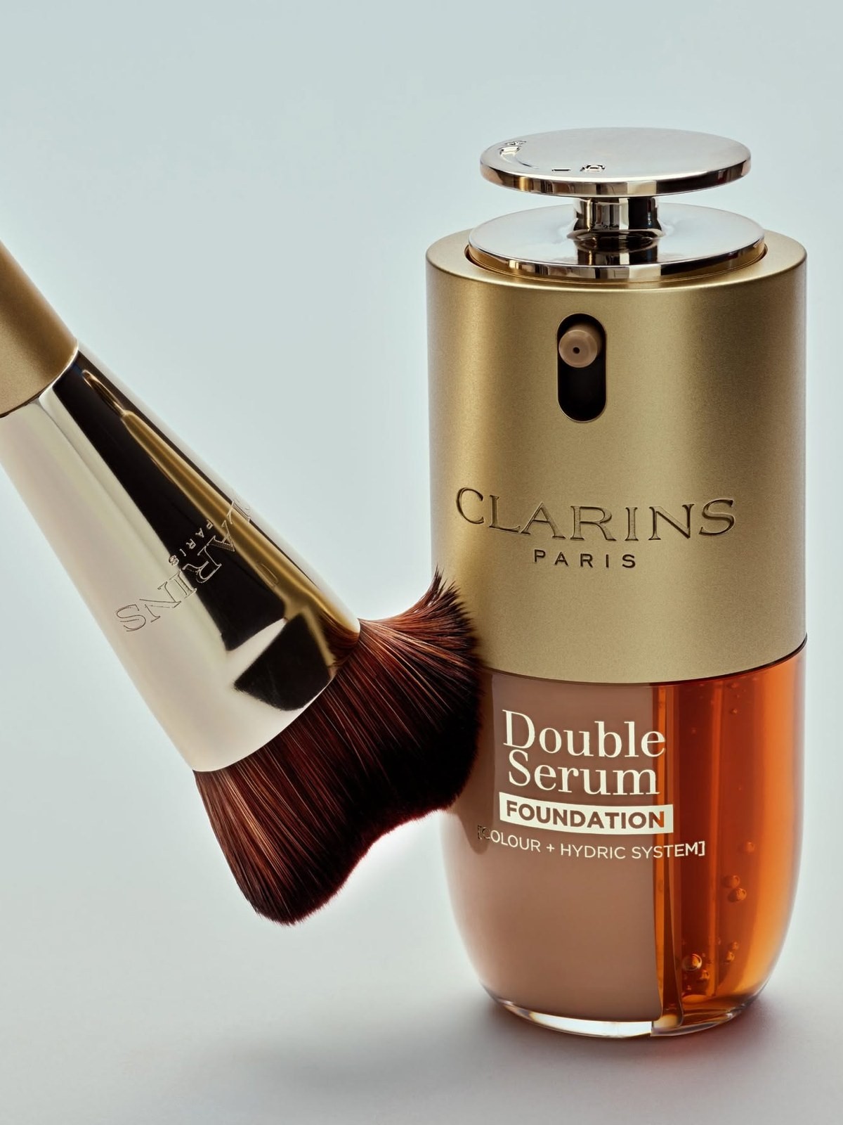 Clarins Double Serum Foundation bottle beside a gold foundation brush