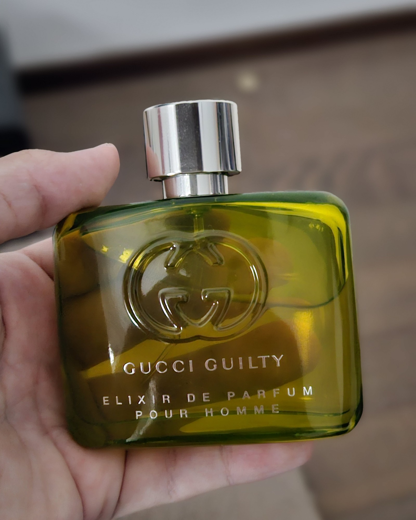 Hand holding a green glass bottle of Gucci Guilty Elixir de Parfum Pour Homme with a silver cap