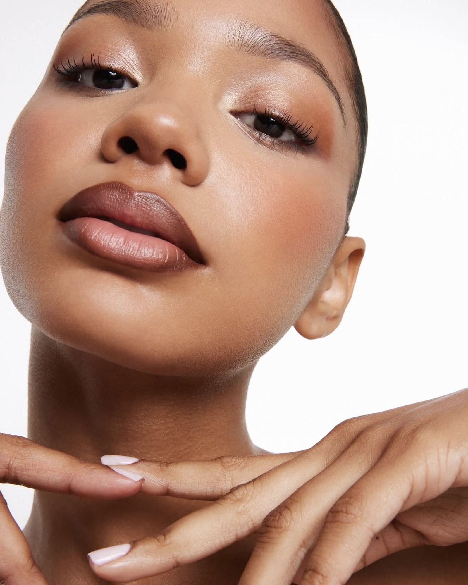 Close-up of a model with a soft brown lip, warm bronze eyes and pale manicured nails