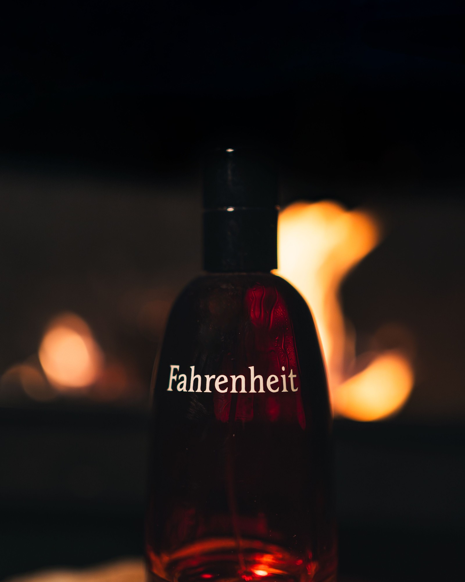 Close-up of a Fahrenheit bottle against a dark background with a blurred fire glowing behind it