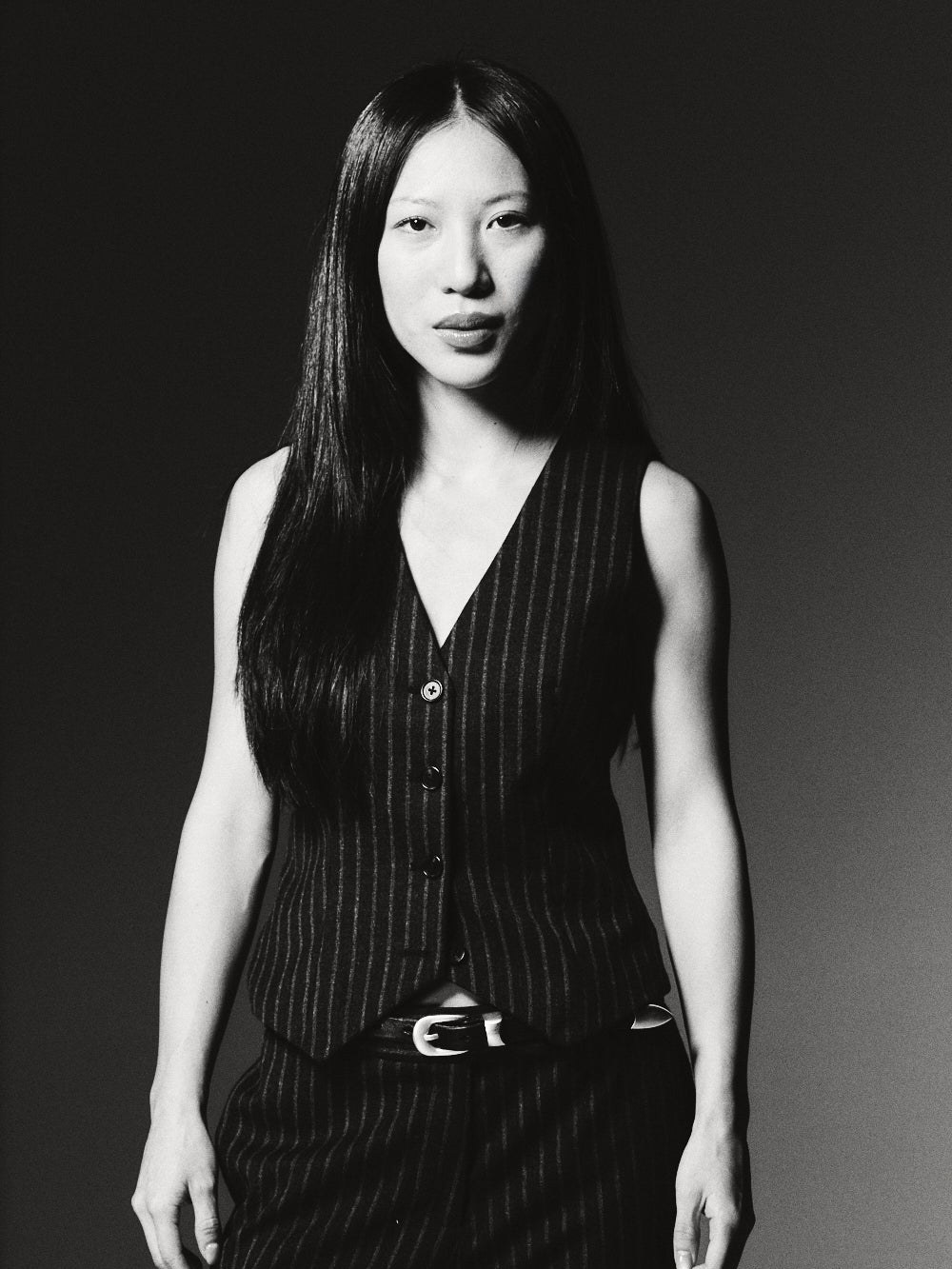 Model in a black pinstripe vest and trousers against a dark studio backdrop