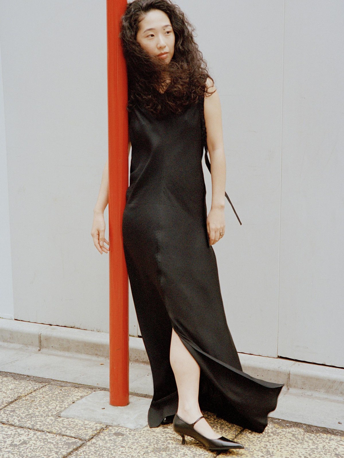 Reina Ogawa Clarke in a black Helmut Lang dress beside a red street pole