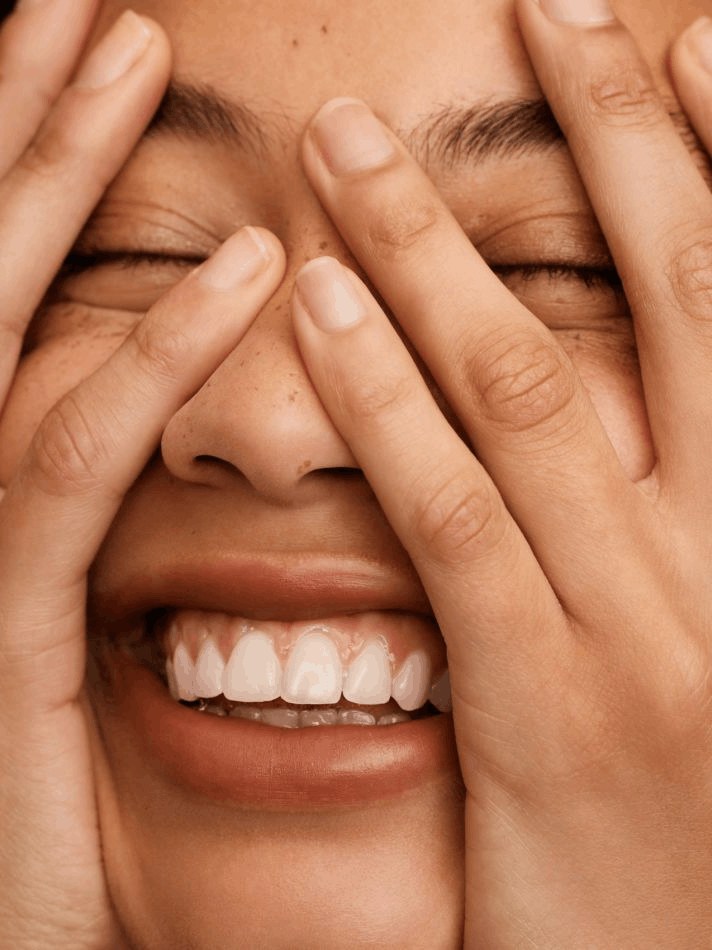 A smiling woman covering her eyes with both hands