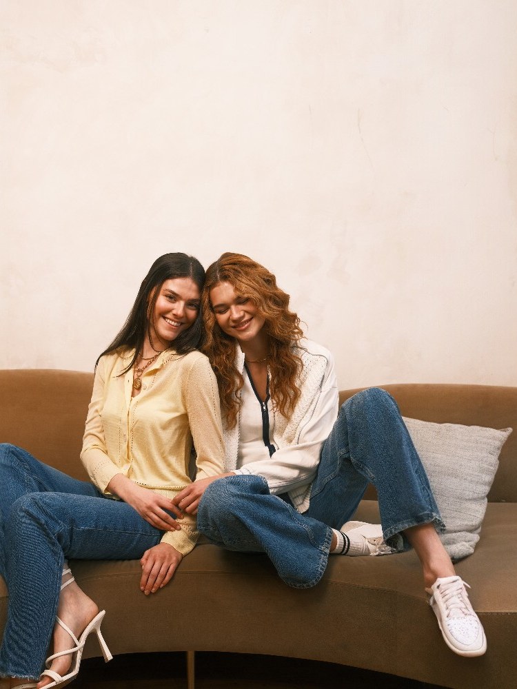 Two models wearing knit layers together on a sofa