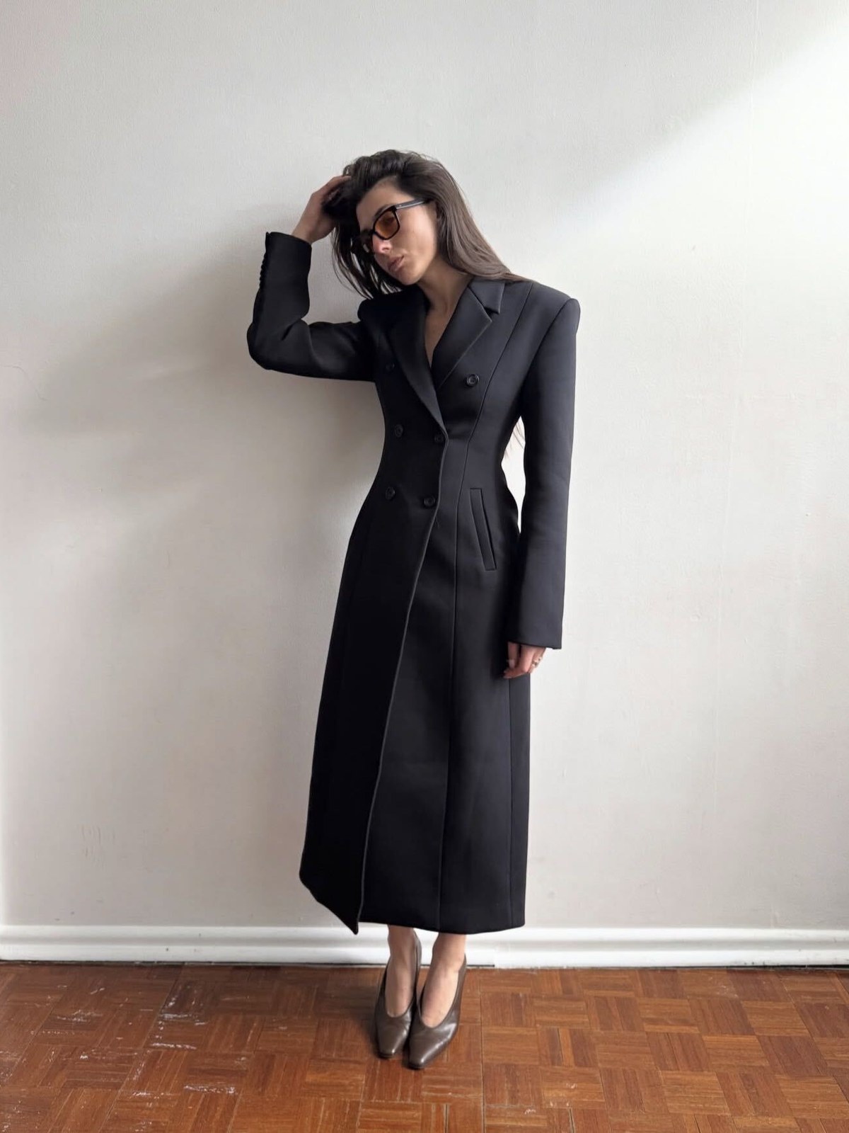 Model in a long dark tailored coat against a pale wall