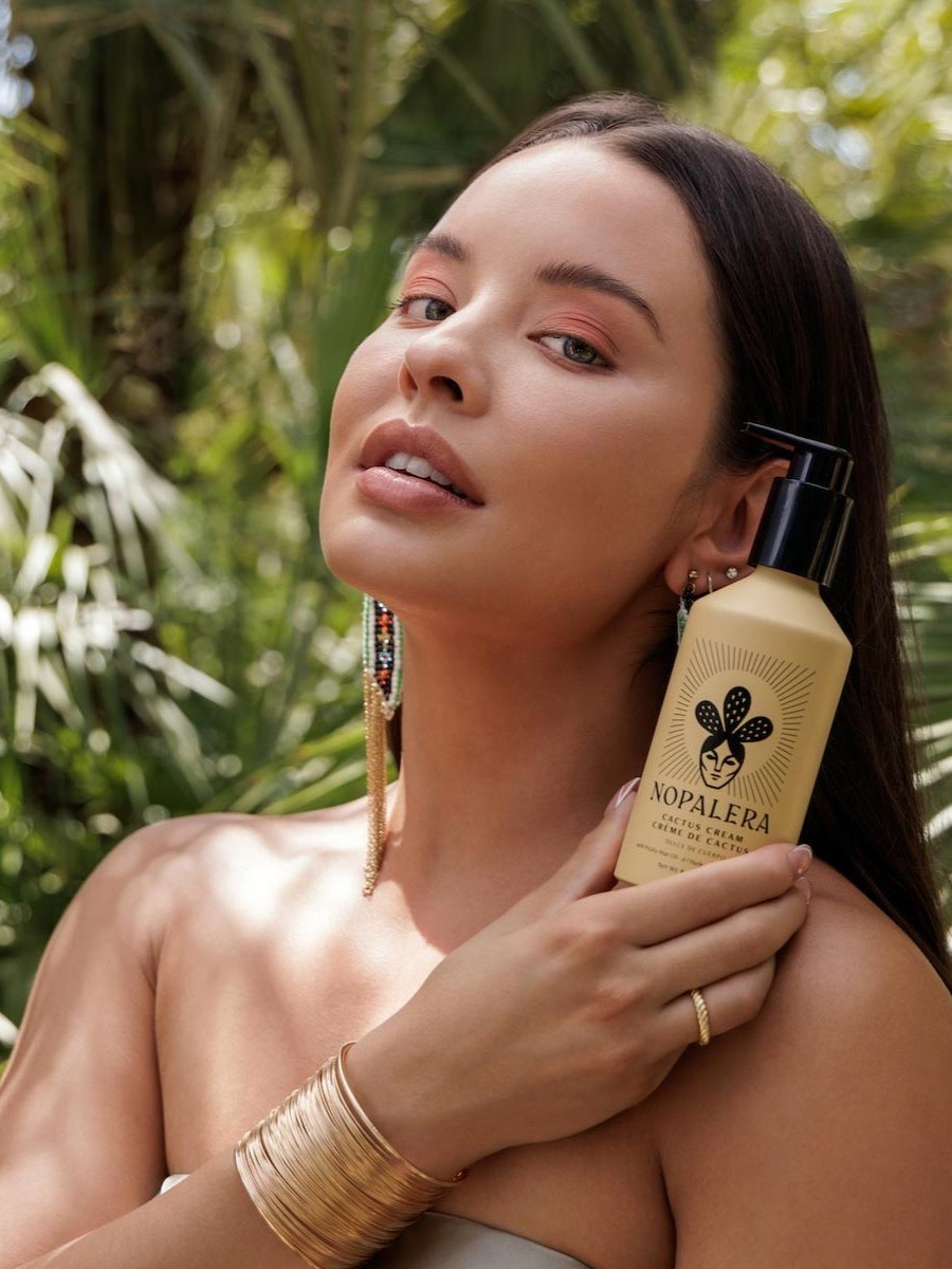 Model holding Nopalera cactus body cream against lush tropical foliage