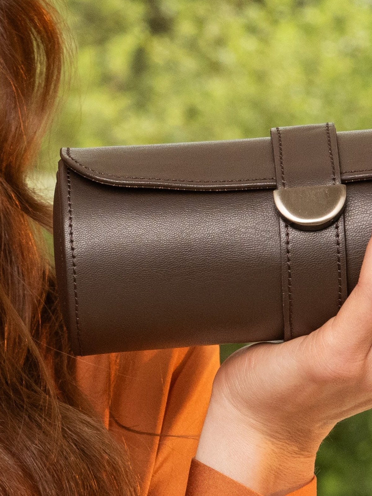 Woman in an orange blouse holding a brown leather watch roll