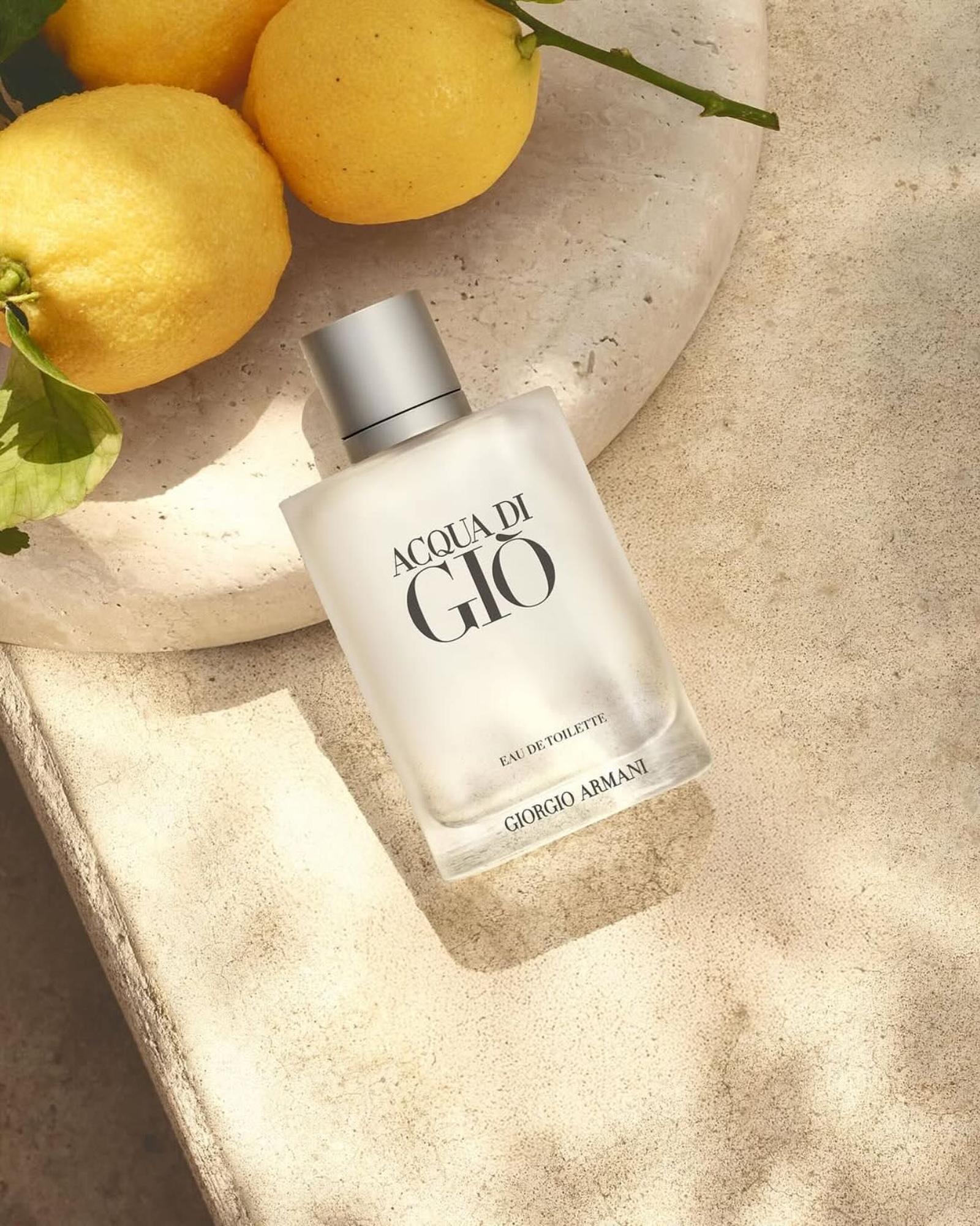 Frosted Acqua di Giò Eau de Toilette bottle resting on a pale stone ledge beside fresh lemons with green leaves.