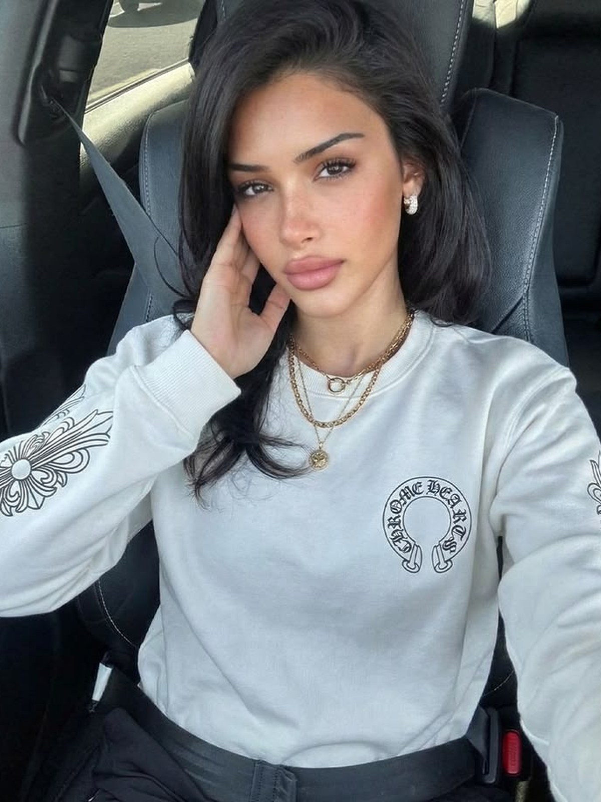 Woman in a white Chrome Hearts sweatshirt with silver cross details and gold chains