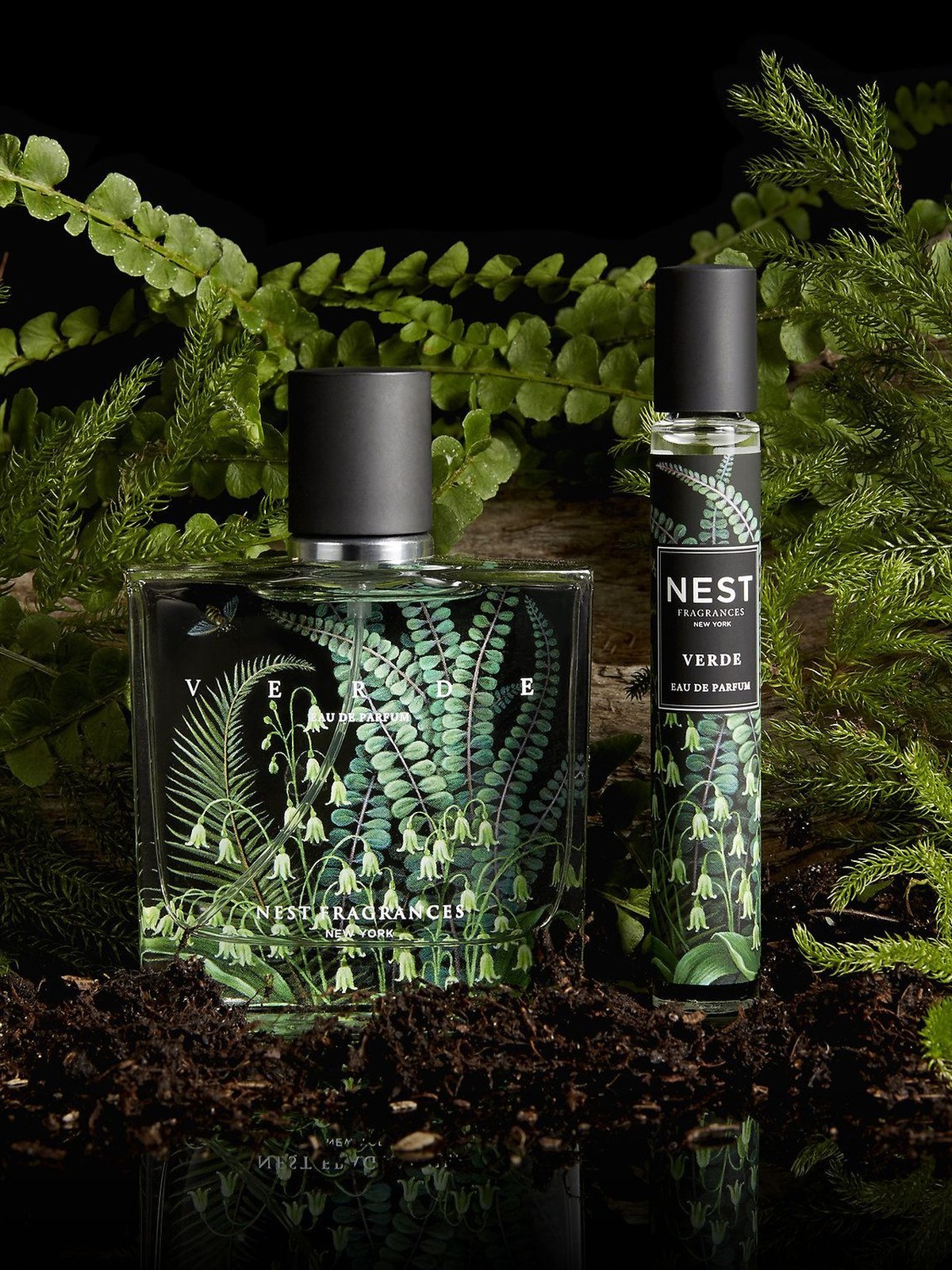 NEST Verde eau de parfum bottle and a rollerball among ferns and dark soil against a black backdrop