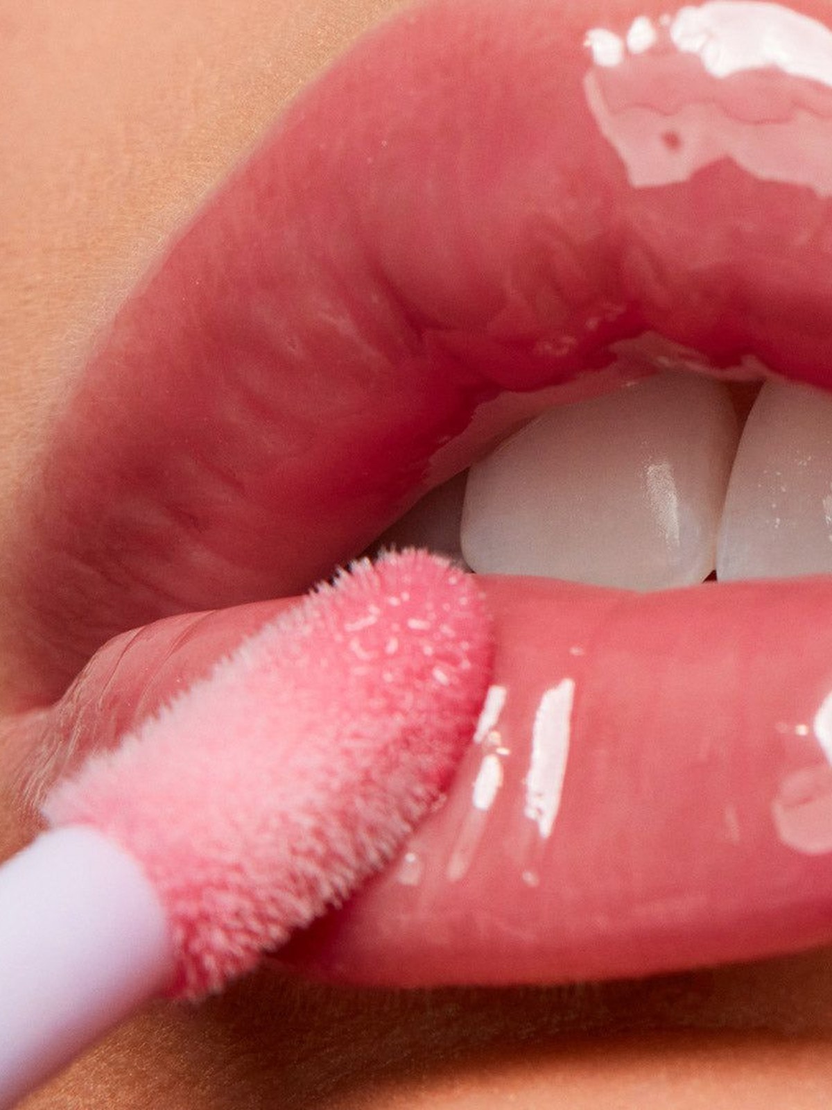 Close up of a soft pink gloss applicator brushing over shiny pink lips