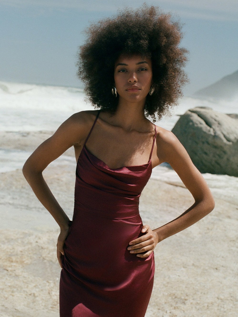 Model in a wine satin gown on a rocky beach