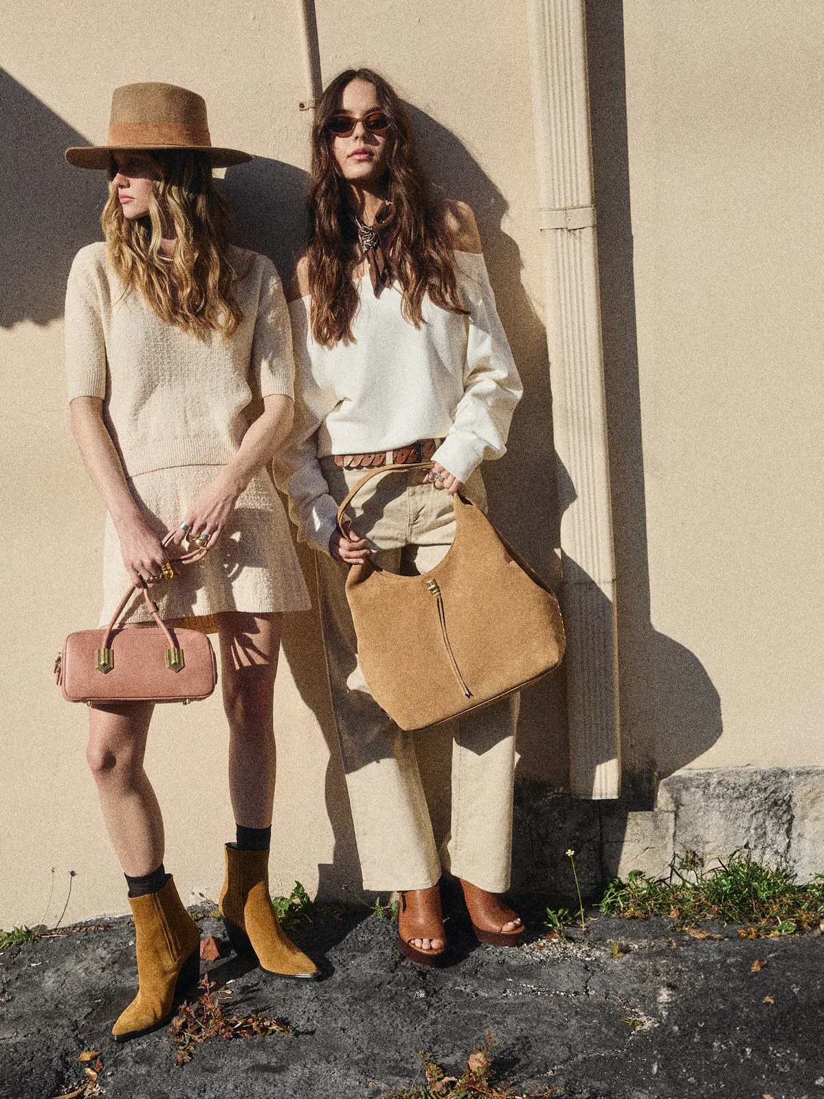 Two models in neutral outfits carrying leather bags outside against a wall