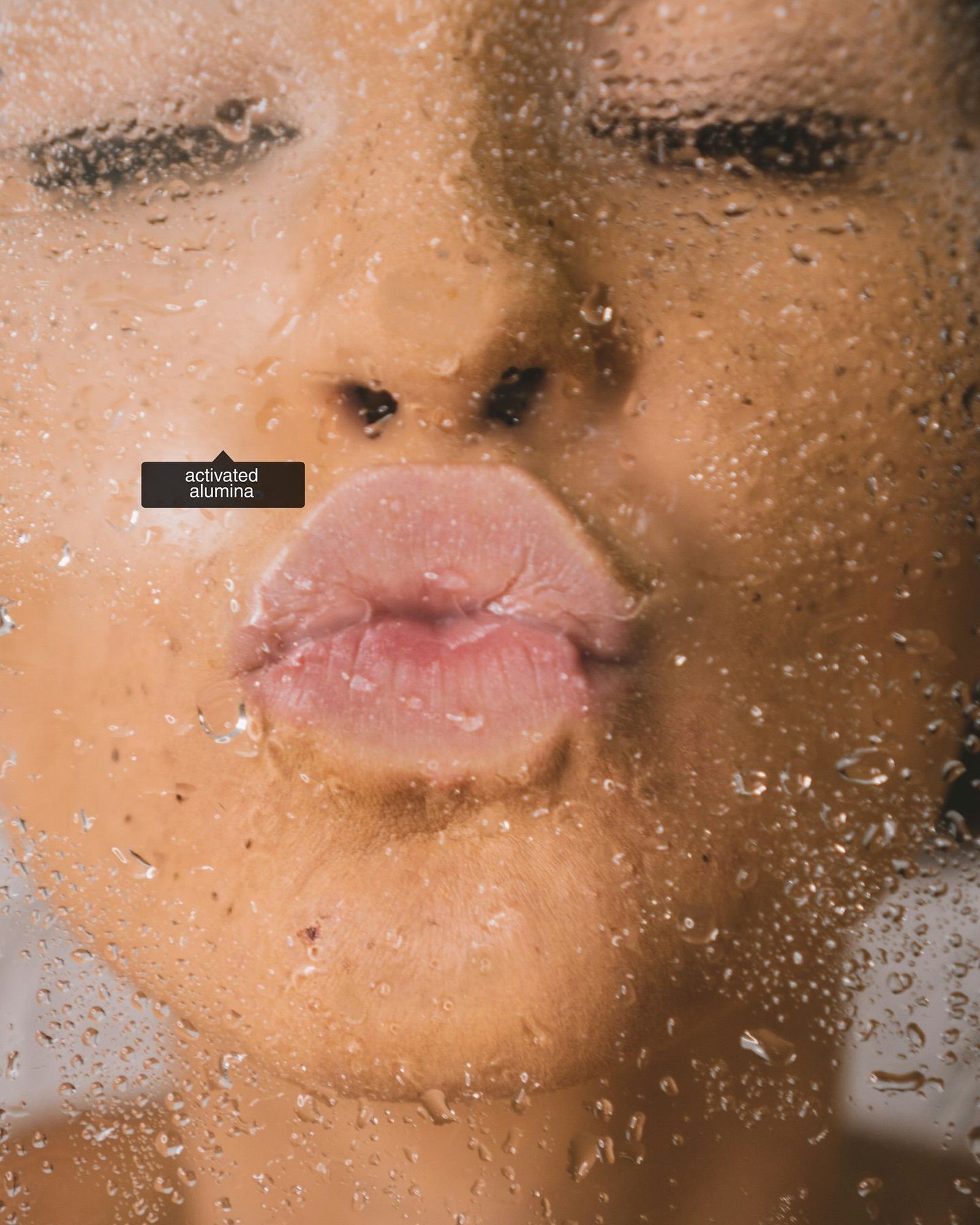 Close-up of a face pressed against a wet shower glass with a label reading activated alumina