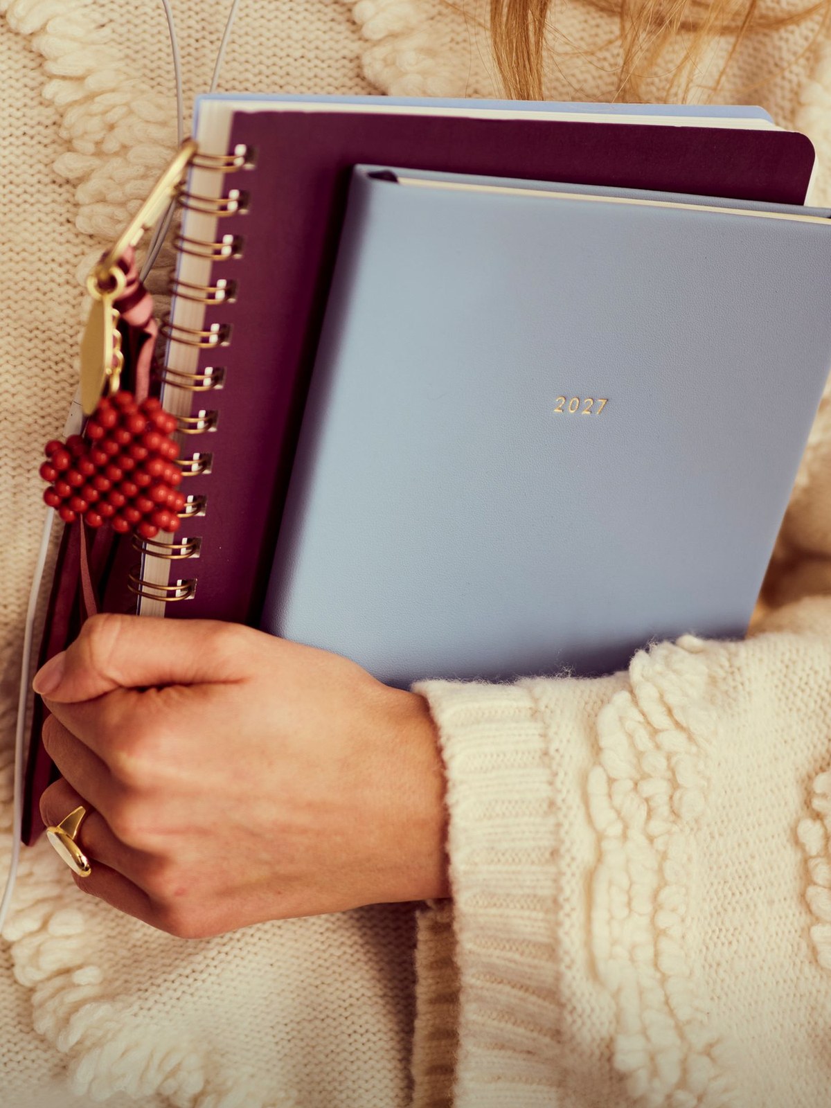 Hands holding Papier planners against a cream knit sweater