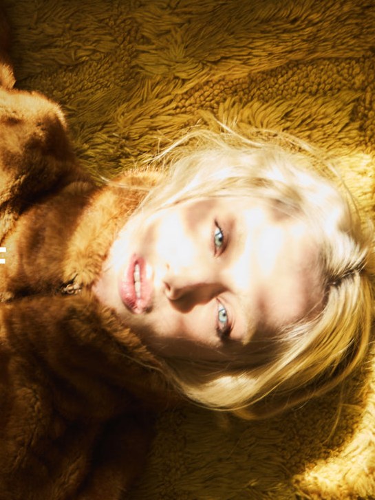 Close campaign portrait of a blonde model reclining against honey-colored textured fabric