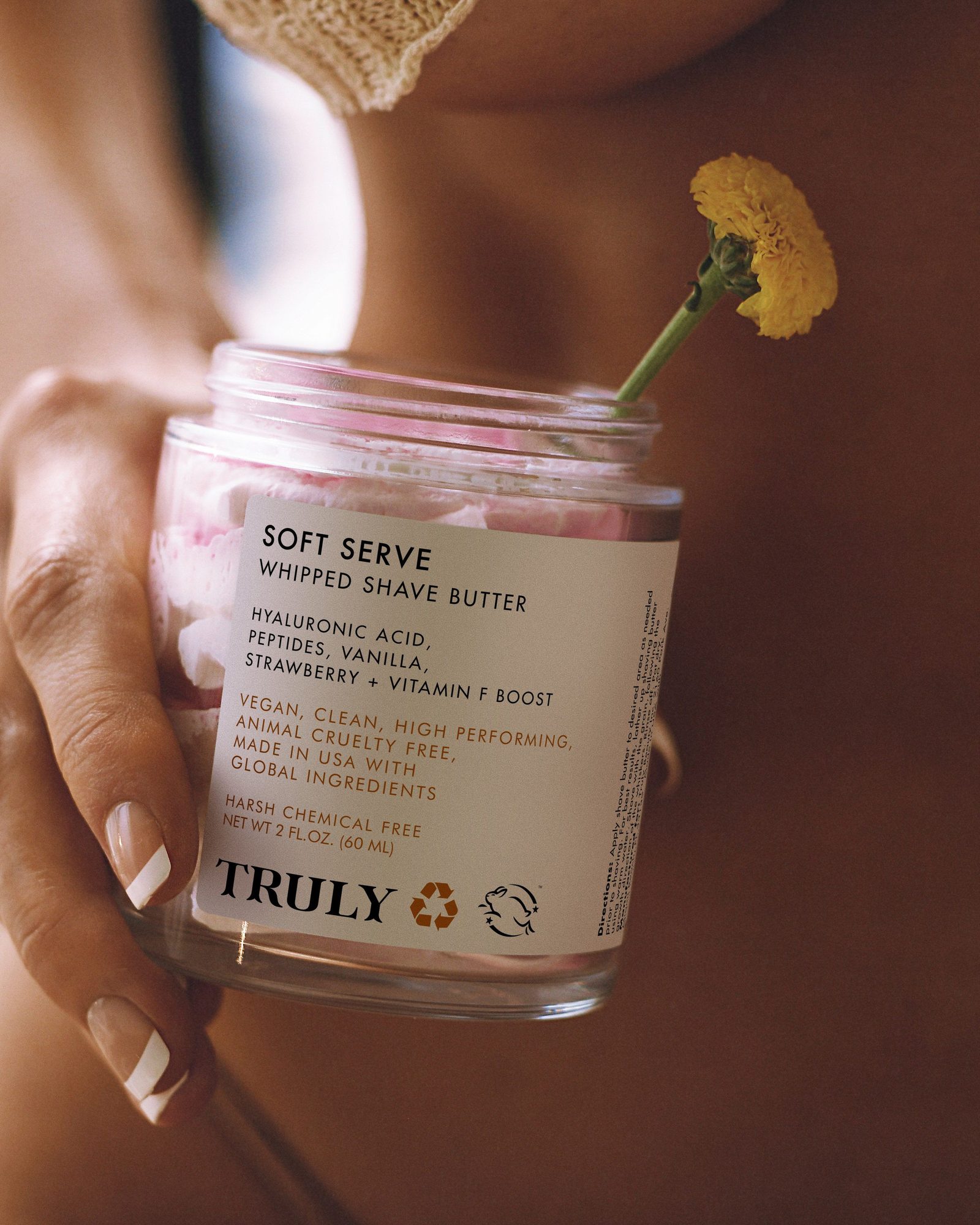 Hand holding a jar of Truly Soft Serve Whipped Shave Butter with a yellow flower tucked beside it
