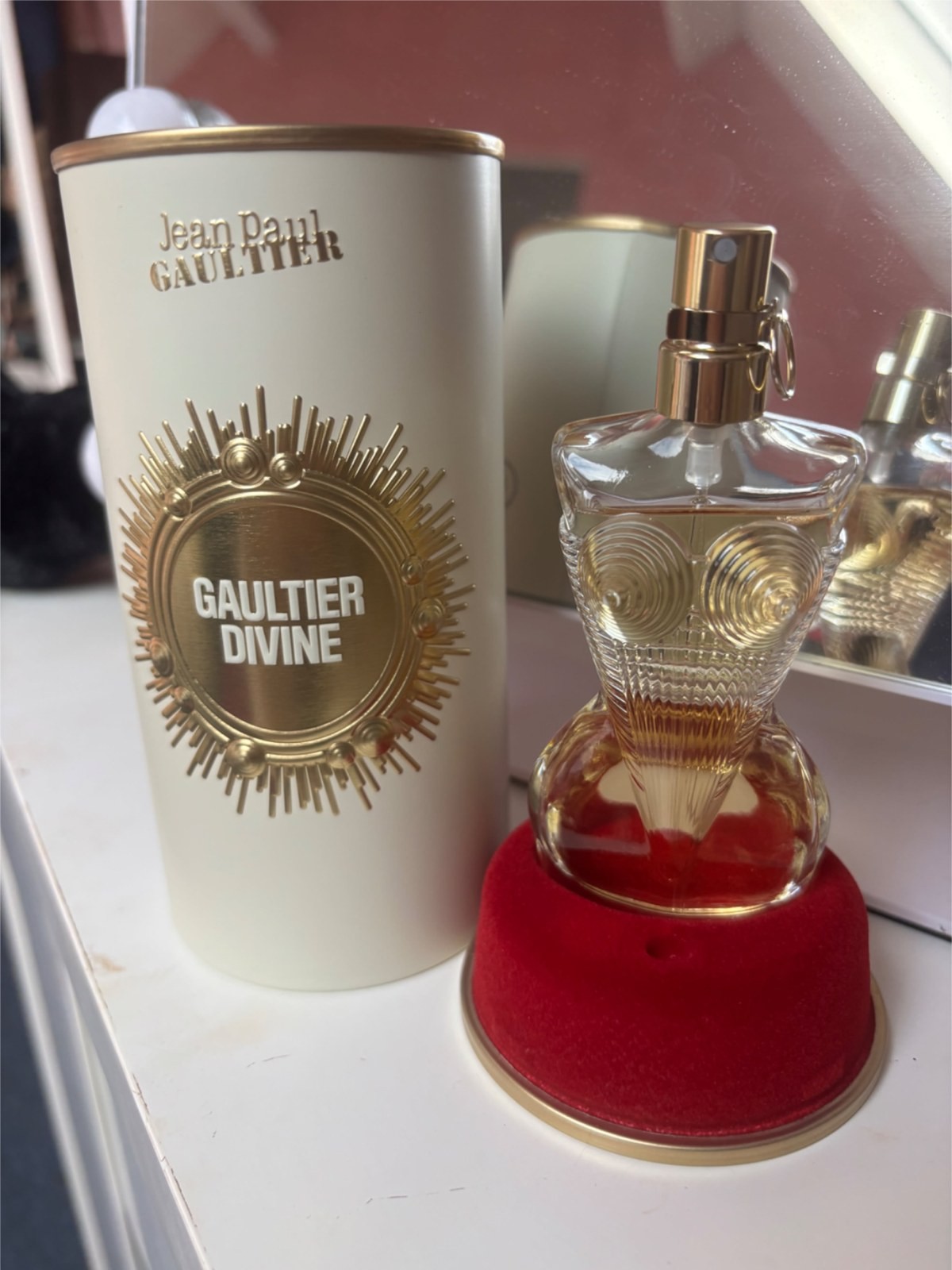 Jean Paul Gaultier Divine perfume bottle and box on a vanity with a red velvet cap