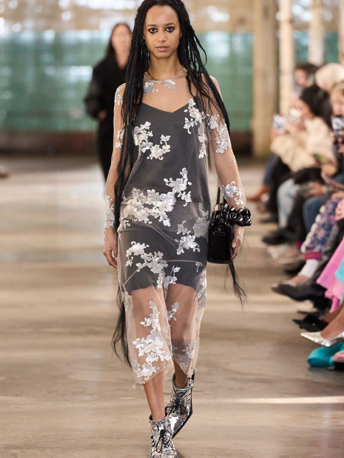 Model in a sheer black dress with pale floral embroidery