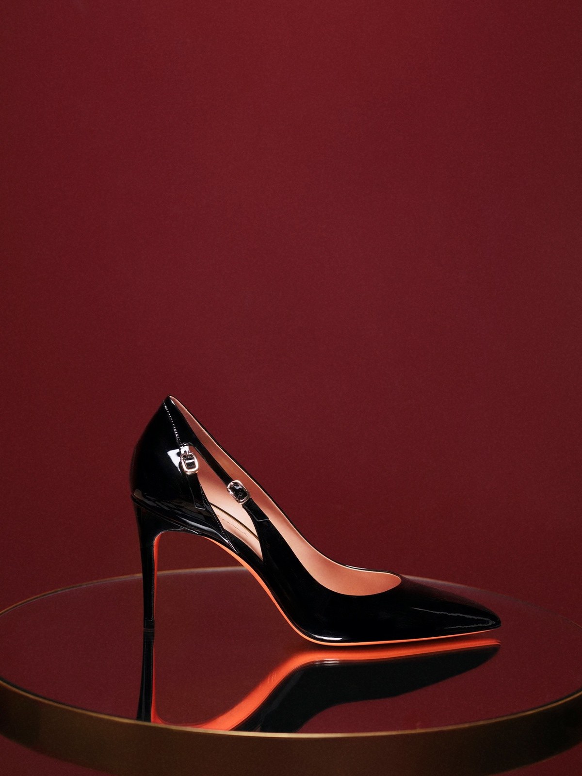 Black patent stiletto pump on a glass table against a deep red wall