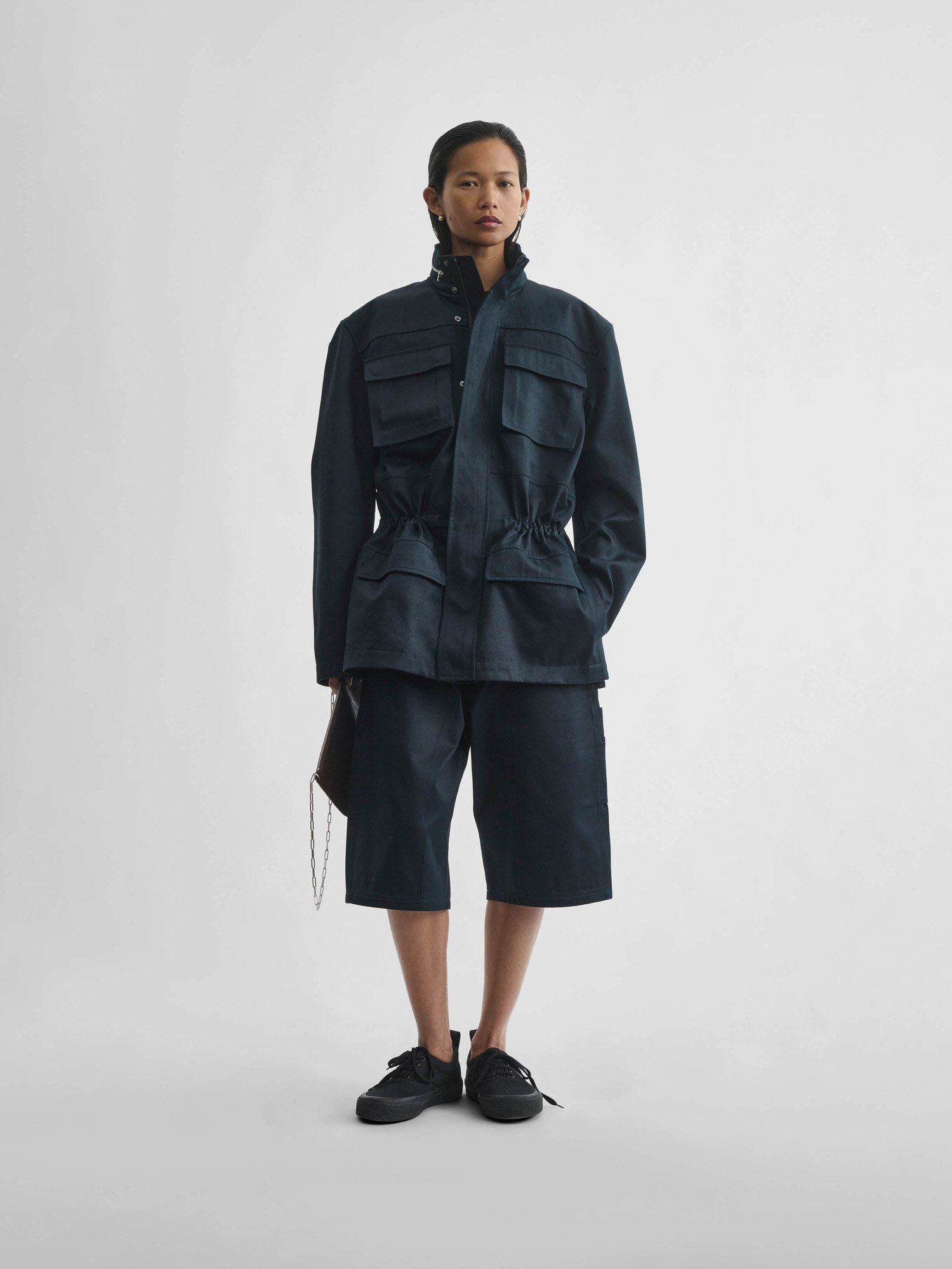 Model in a black ink cotton utility jacket and shorts with flat shoes