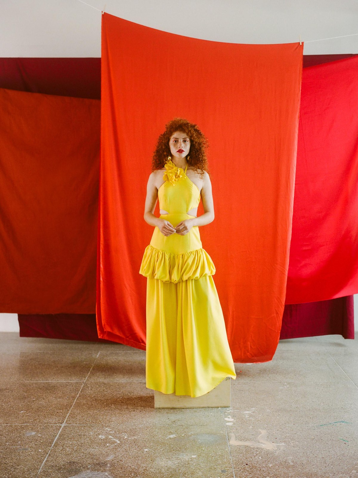 A woman in a bright yellow dress stands before red curtains in Ceremonia's Latinx Heritage Month campaign.