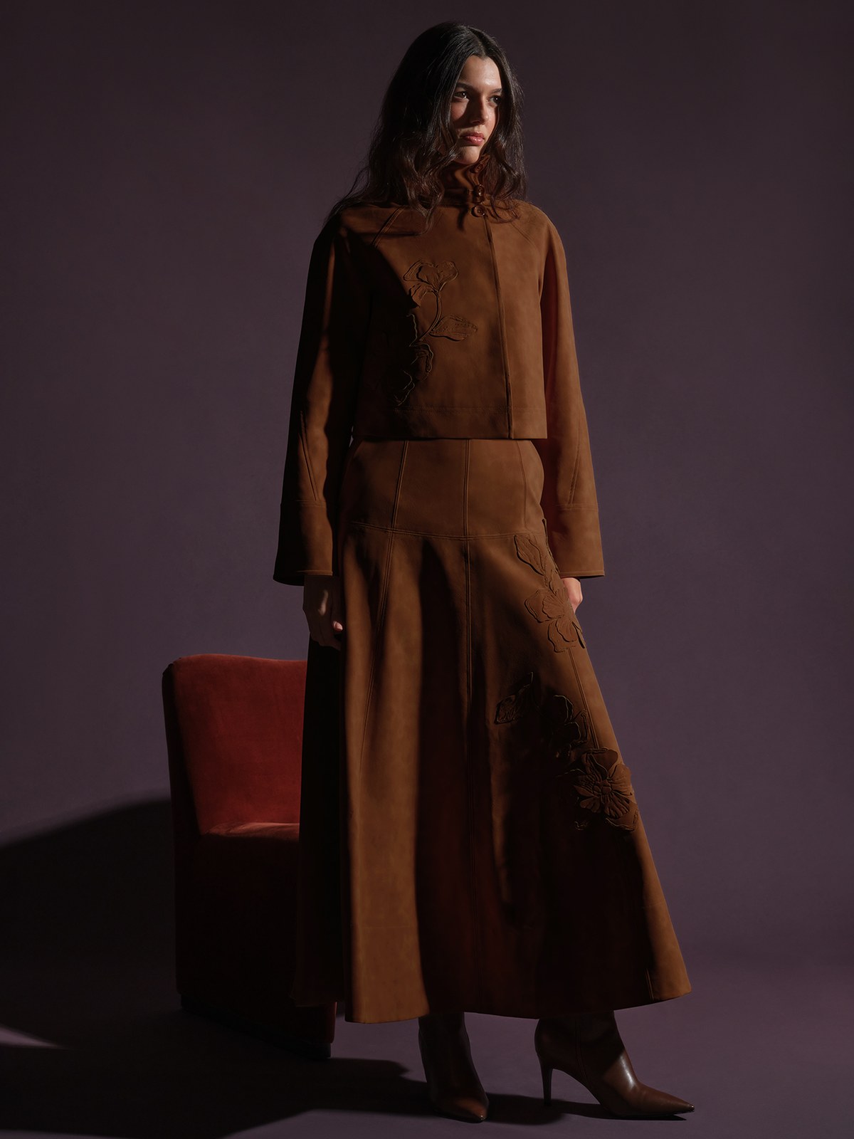 Model in a brown embroidered two piece set beside a red chair
