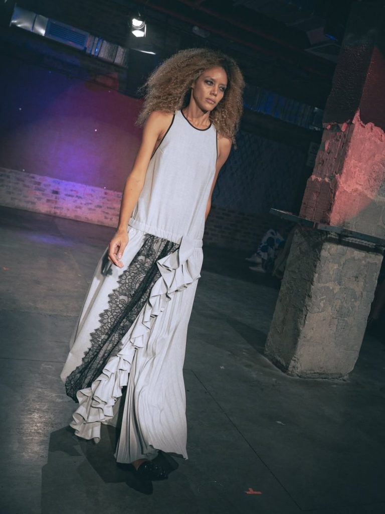 Runway model in a flowing white dress with a dark lace panel