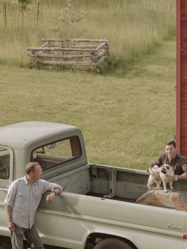 Two MALIN+GOETZ founders with a dog beside a vintage pickup in a rural setting