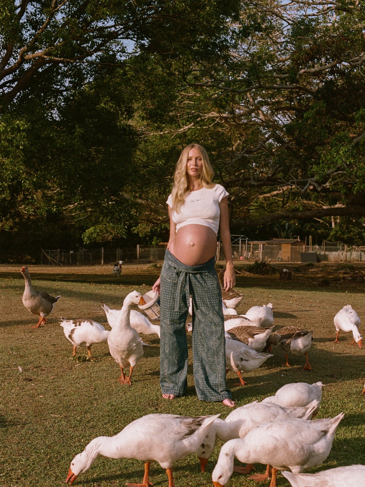 Pregnant model Bee Cooper standing in a field among white geese in a BUMPSUIT x Spell campaign.