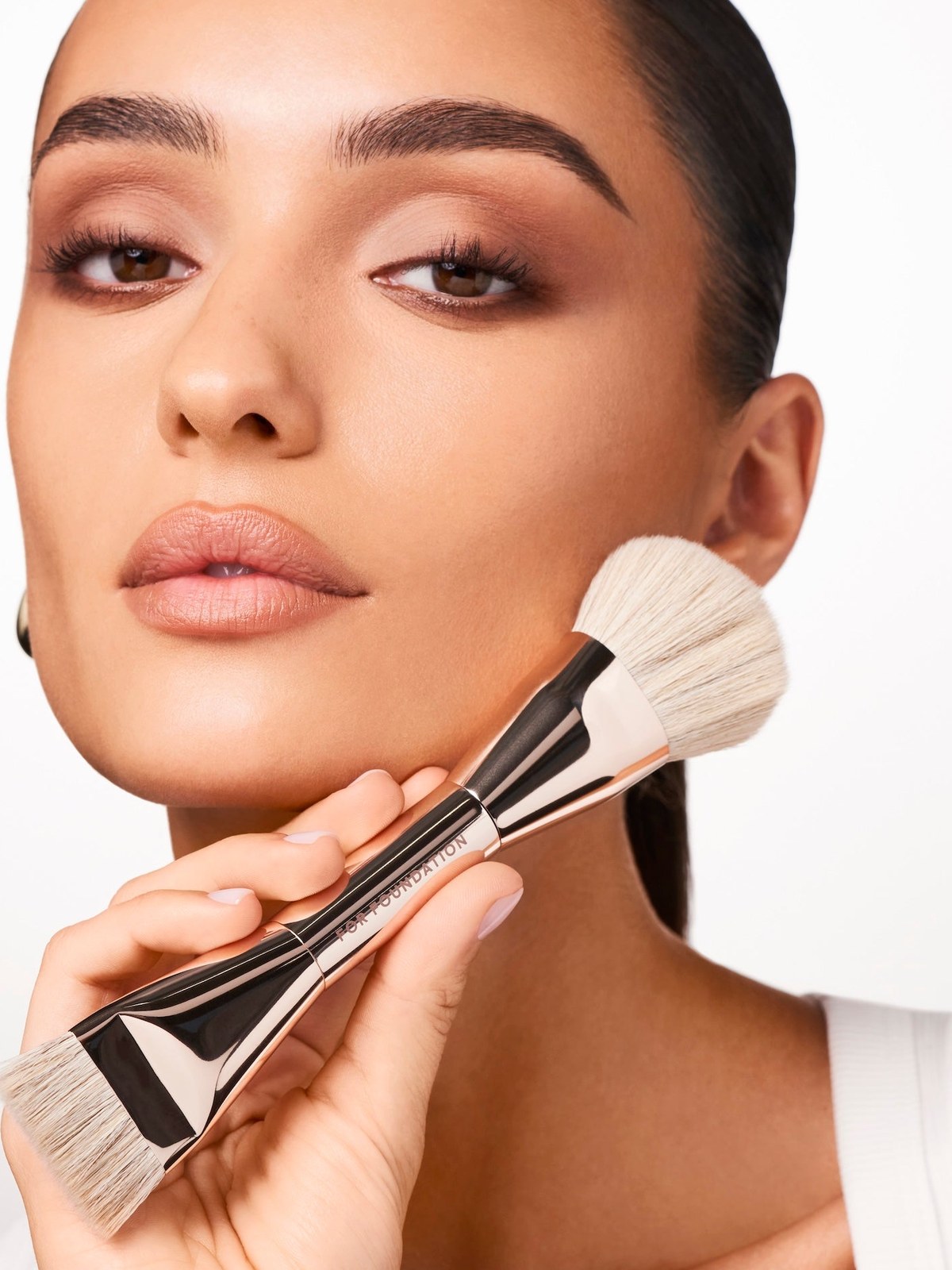 Model with soft neutral eye holding a dual ended blush brush to her cheek