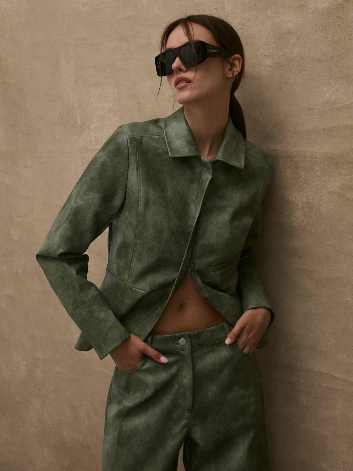 Model in an olive jacket and matching trousers against a stone wall