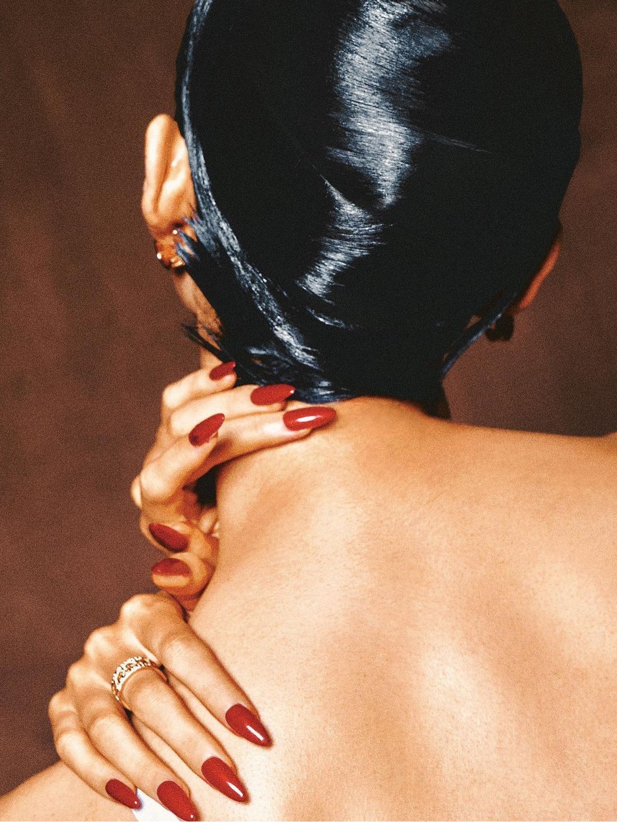 Glossy red almond press-on nails on a hand resting on a bare shoulder