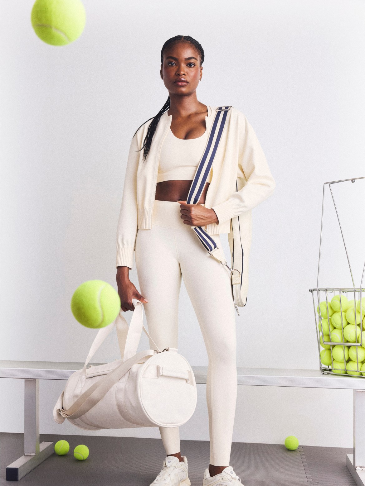 Model in cream activewear with tennis balls and a racket bag