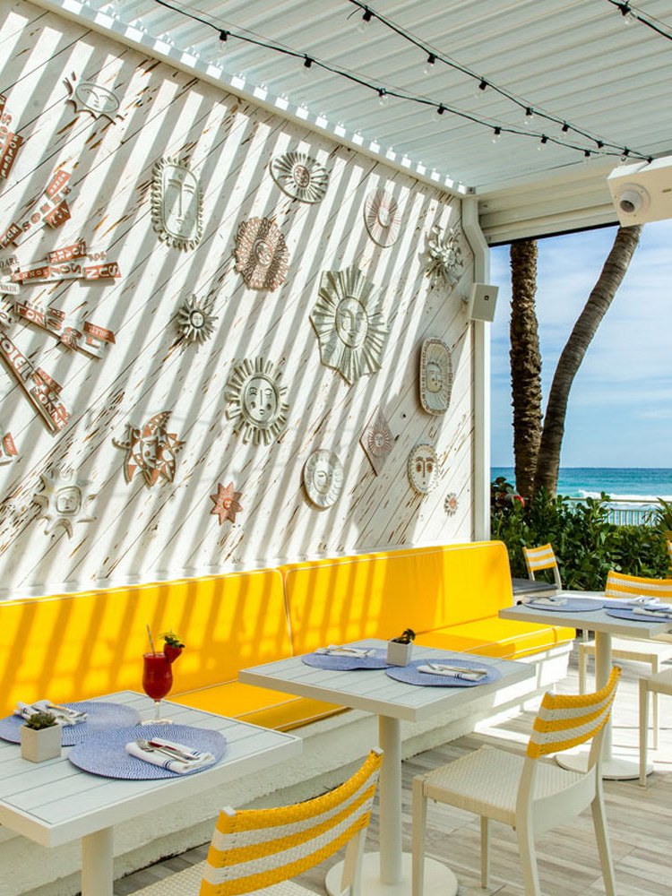 Sunny oceanfront dining terrace with yellow banquette seating