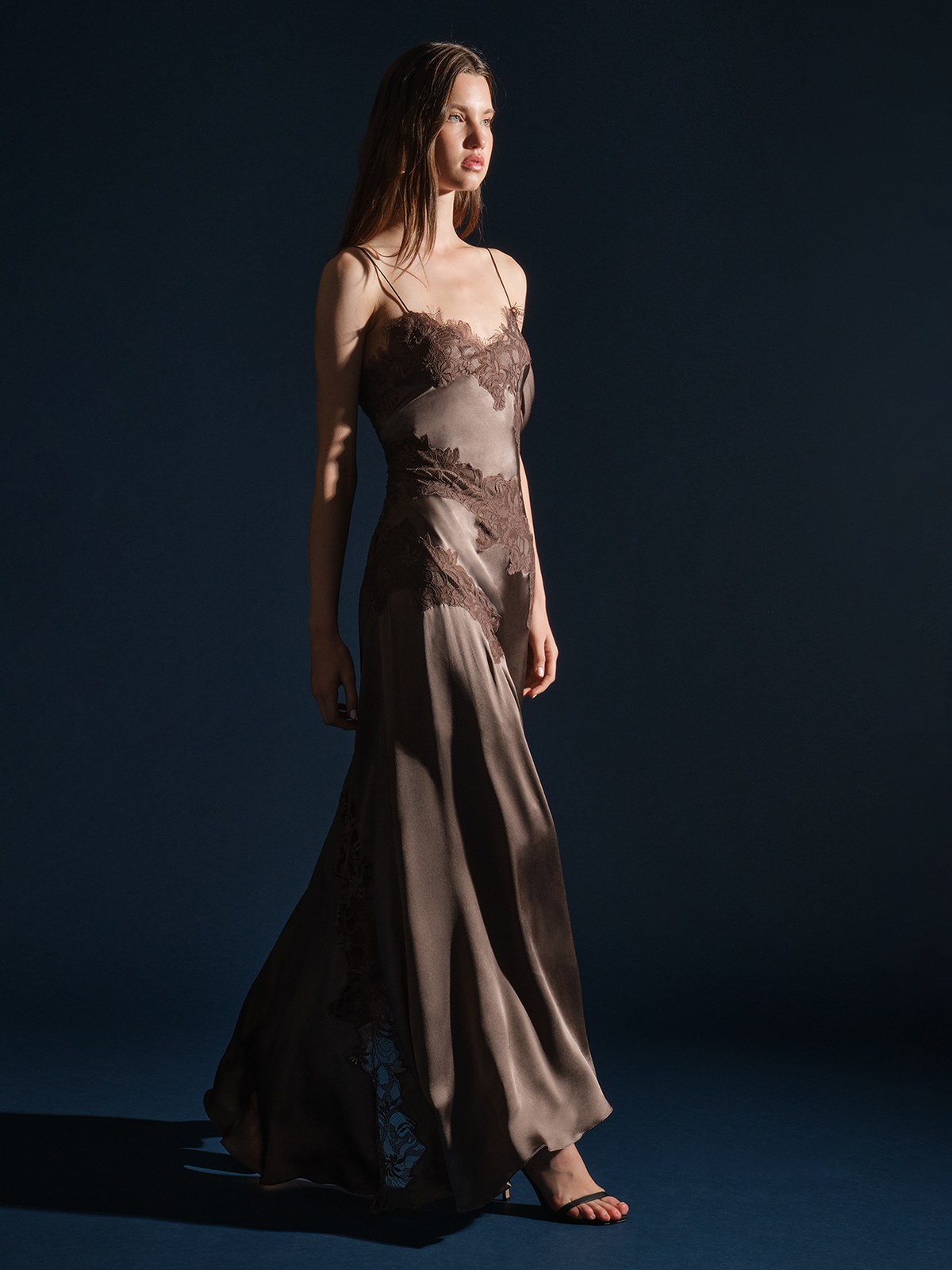 Model in a taupe lace trim gown against a deep blue studio background