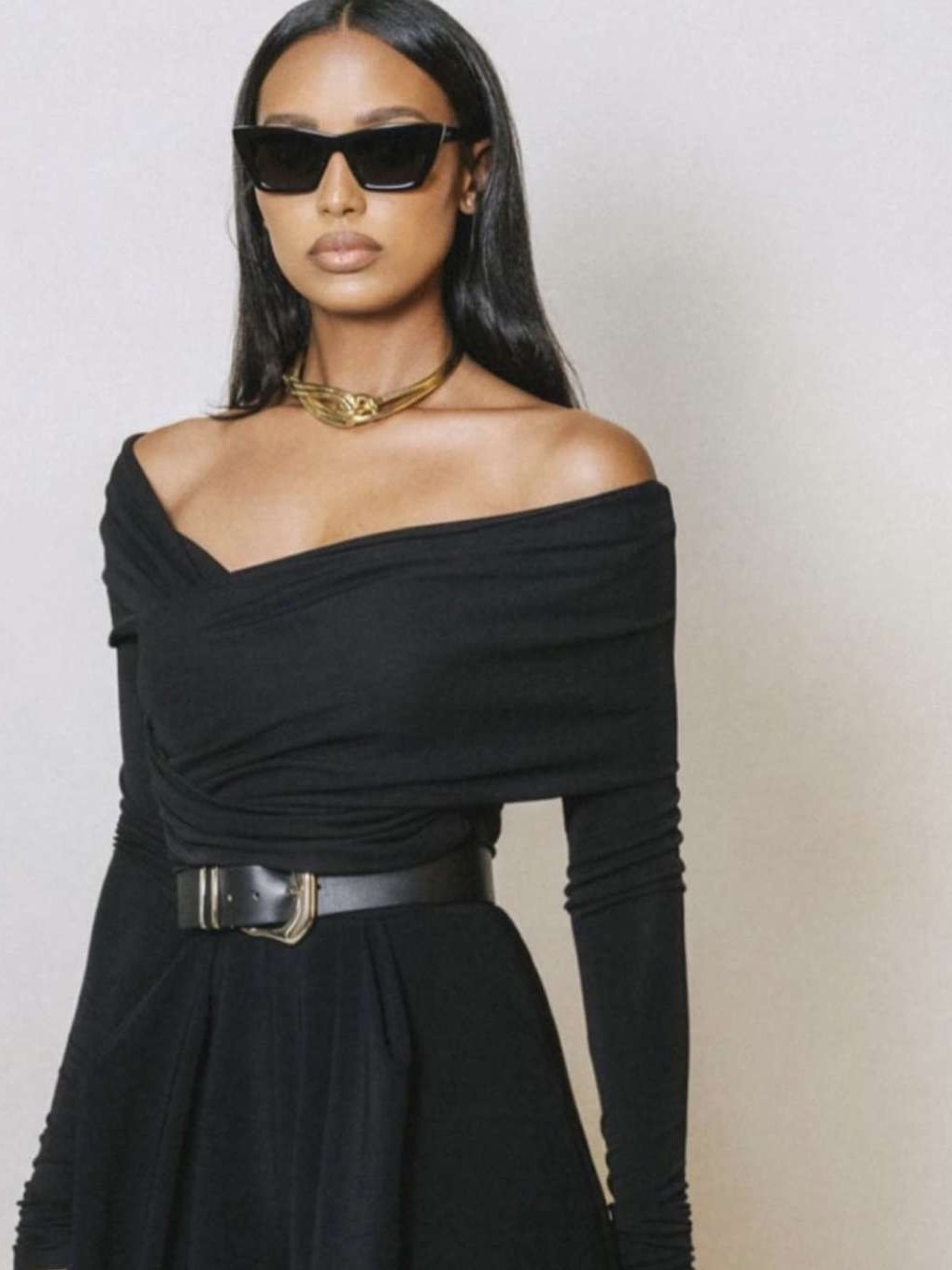 Model in a black off-shoulder look with a wide belt against a light studio wall
