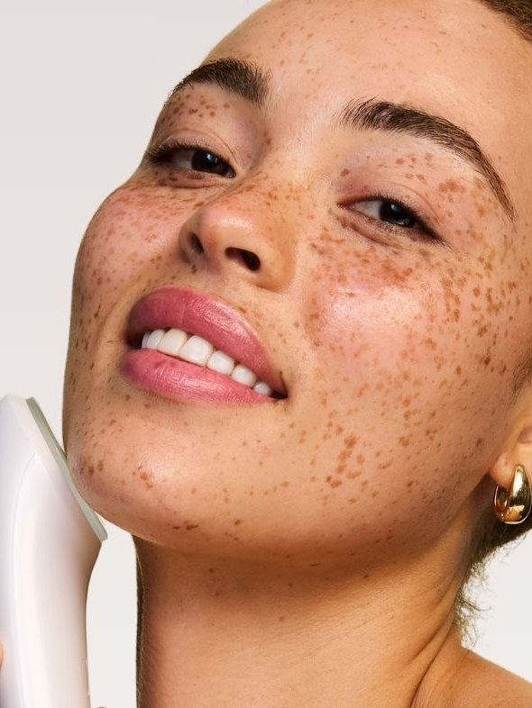 Freckled model smiling while holding a white Solaris facial tool to her cheek