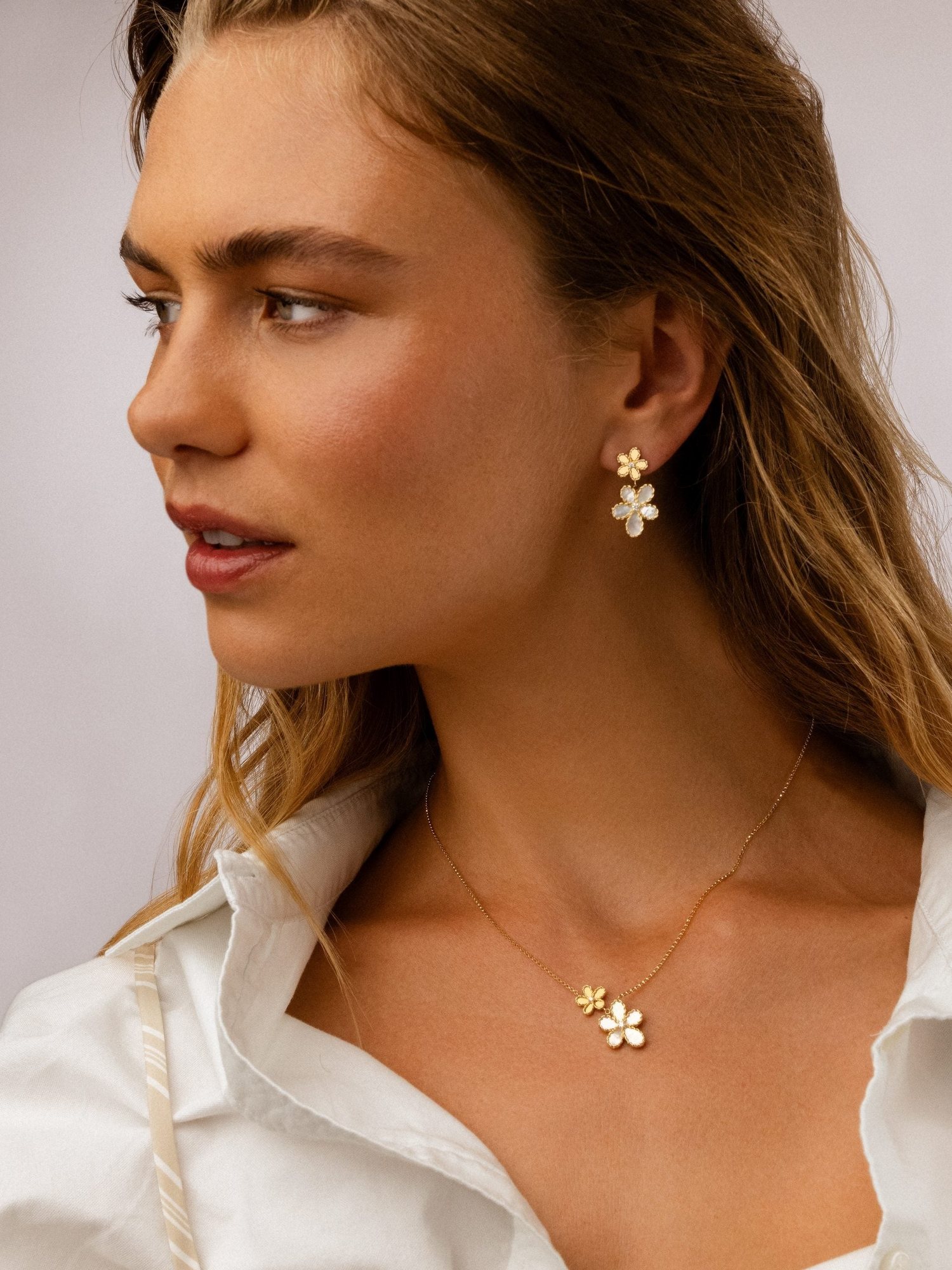 Blonde model in profile wearing Roberto Coin flower earrings and pendant with a white shirt