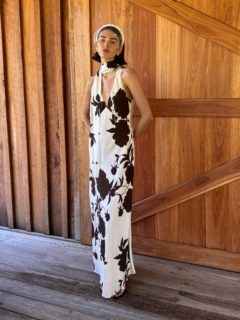 Model in a black and white floral MINKPINK dress standing by a wooden wall