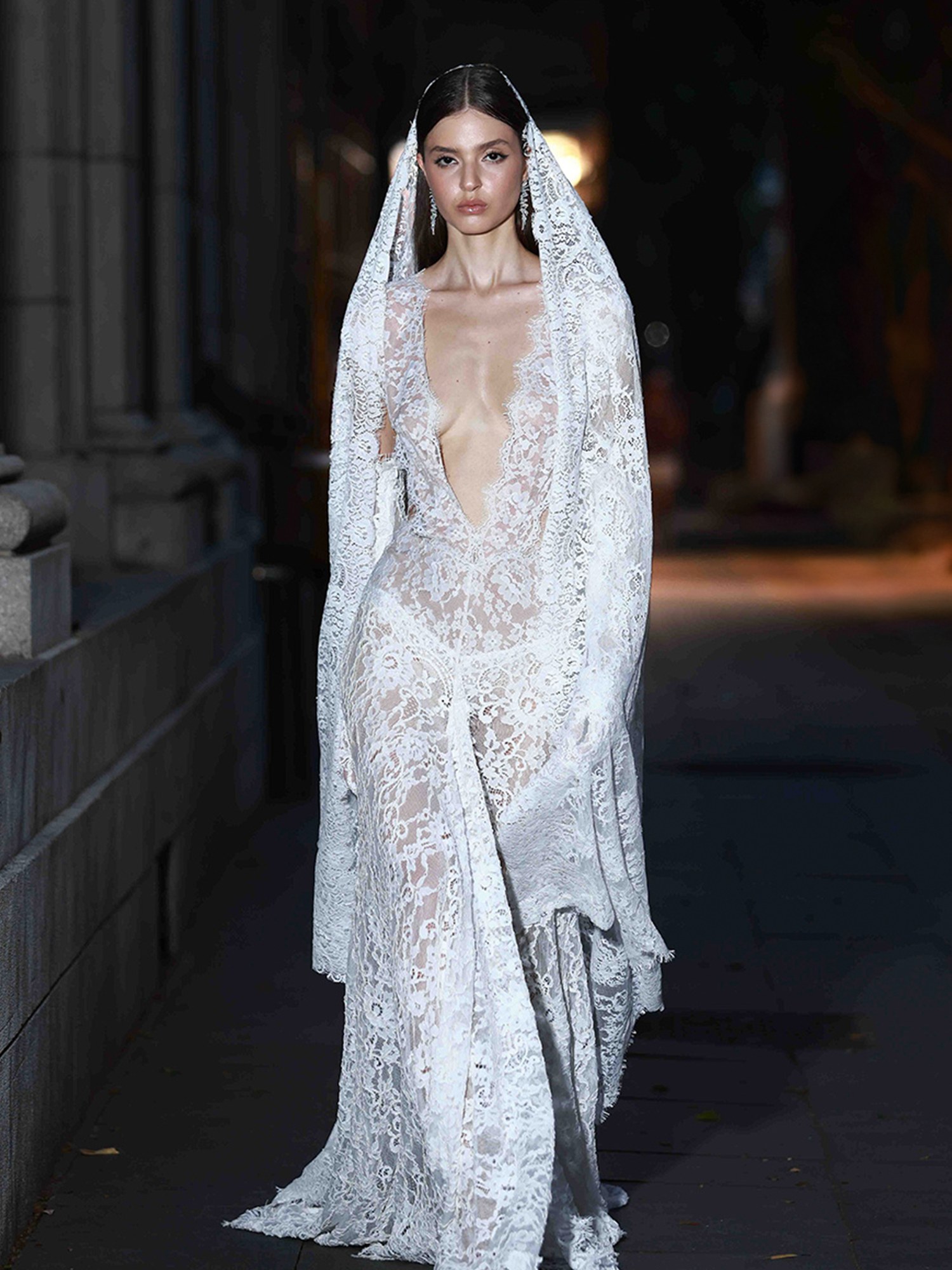 Bridal runway look with a sheer lace gown and veil on a dark city street